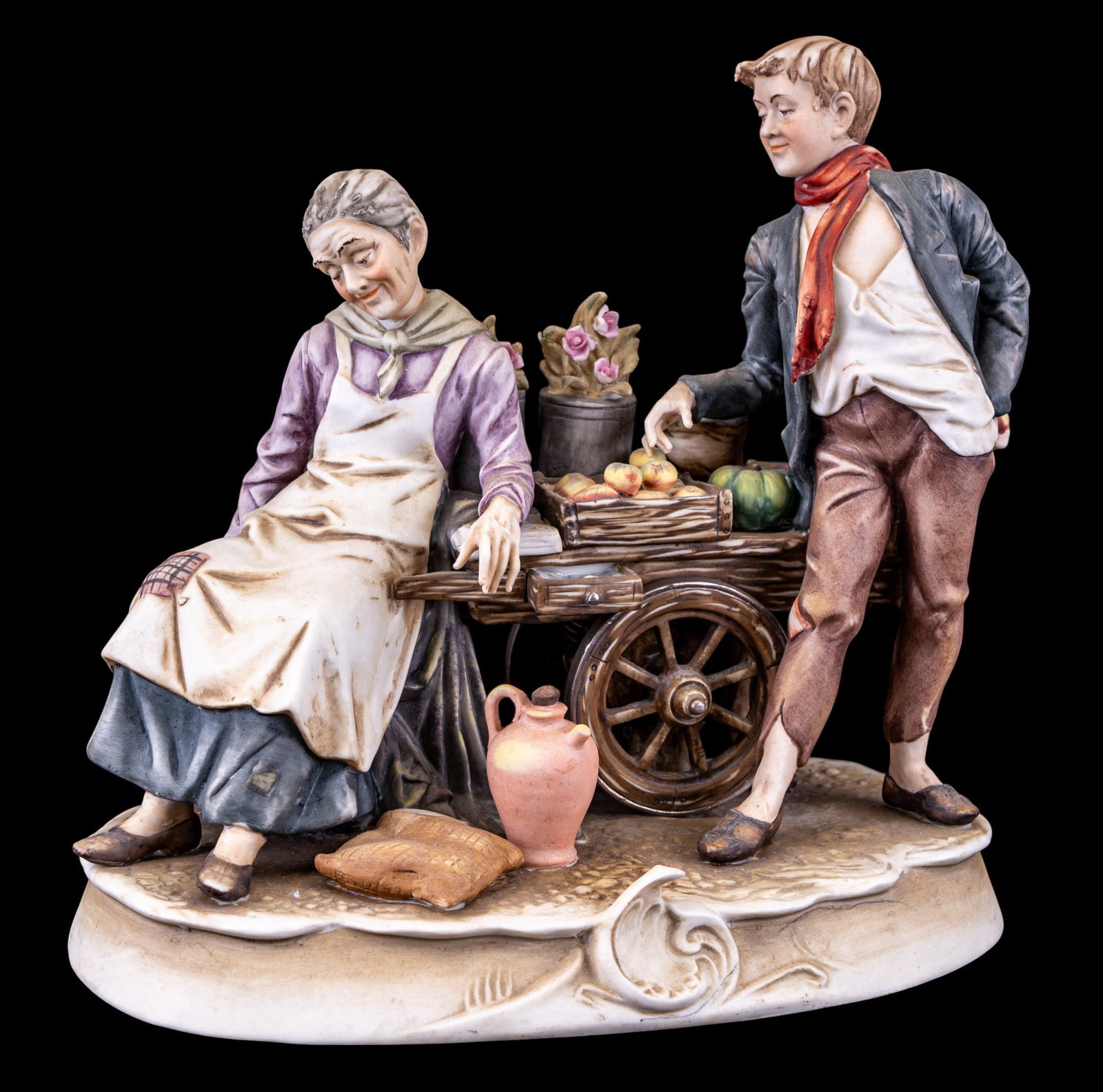 Arnart Porcelain Figural Sculpture: Arnart hand-painted porcelain figural group depicting an elderly female market vendor and young man posed beside a cart filled with fruit. Marked to underside. Measures approx. 10" W x 9.75" H.