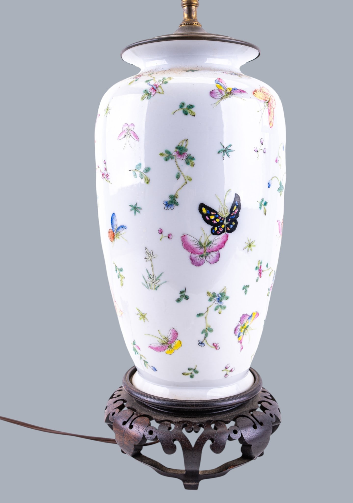 Chinese Famille Rose Canton Porcelain Lamp: A Chinese export Famille Rose Canton porcelain table lamp featuring a carved wooden base, depicting flowers and butterflies. Measures approx. 19" H to the socket, 29" H to the finial.