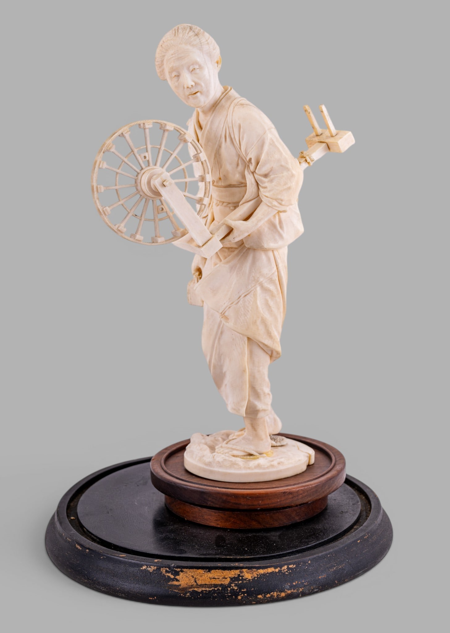 Antique Japanese Figure of Woman w/ Spinning Wheel: Antique Japanese carved natural material figural sculpture depicting a woman operating a traditional spinning wheel. Mounted on shaped wooden display base. Condition is as seen in photography.