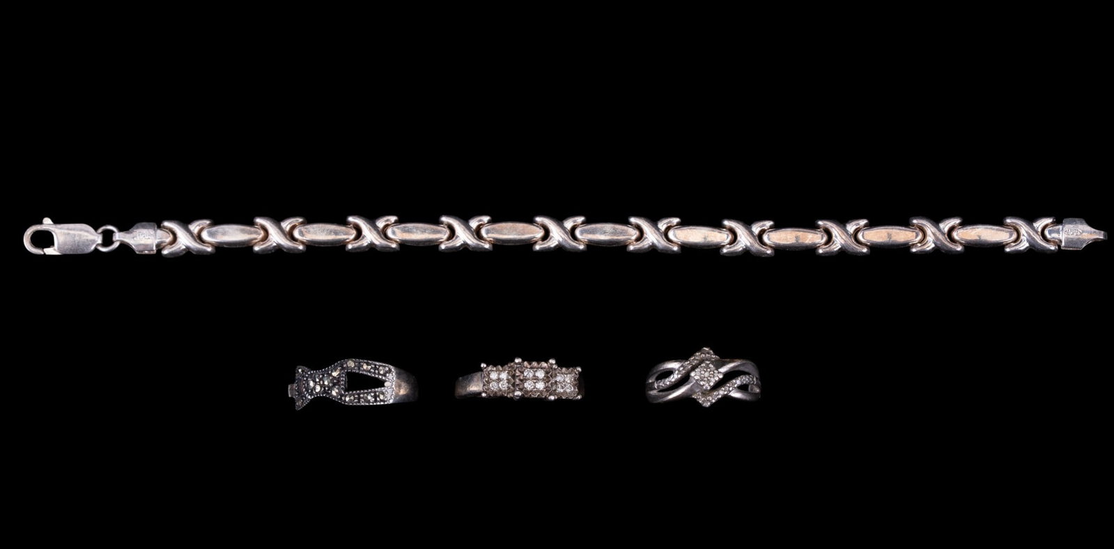 Sterling Silver Rings and Bracelet: A collection of sterling silver jewelry including an Italian XOXO tennis bracelet, a vintage marcasite buckle motif ring, a facet cut stone ring signed 'SUN', and a Kenneth David diamond ring. Ring si