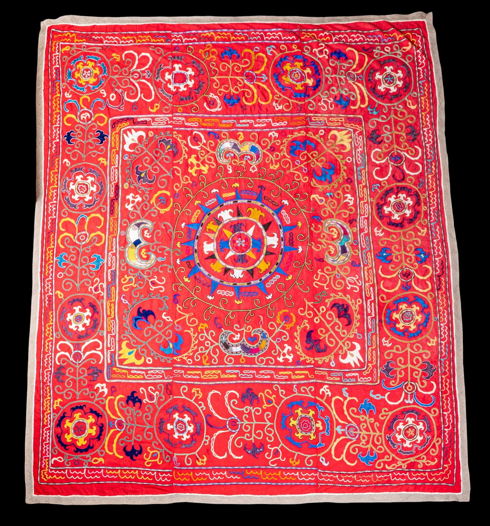 Asian Uzbek Suzani Colorful Embroidered Textile: Large-scale Central Asian Uzbek Suzani hand-embroidered textile. Features dense, vibrant needlework across red field in a regional color palette, framed by distinct quilted border with delicate