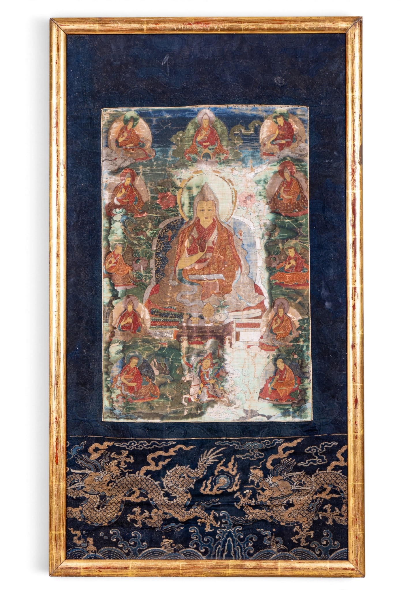 17/18th C Thangka with Silk Dragon Border: 17th - 18th Century Tibetan/Chinese Thangka featuring beautiful detailed painted scenes on cotton from the life of Buddha mounted to blue silk with with an embroidered dragon in a distressed gold