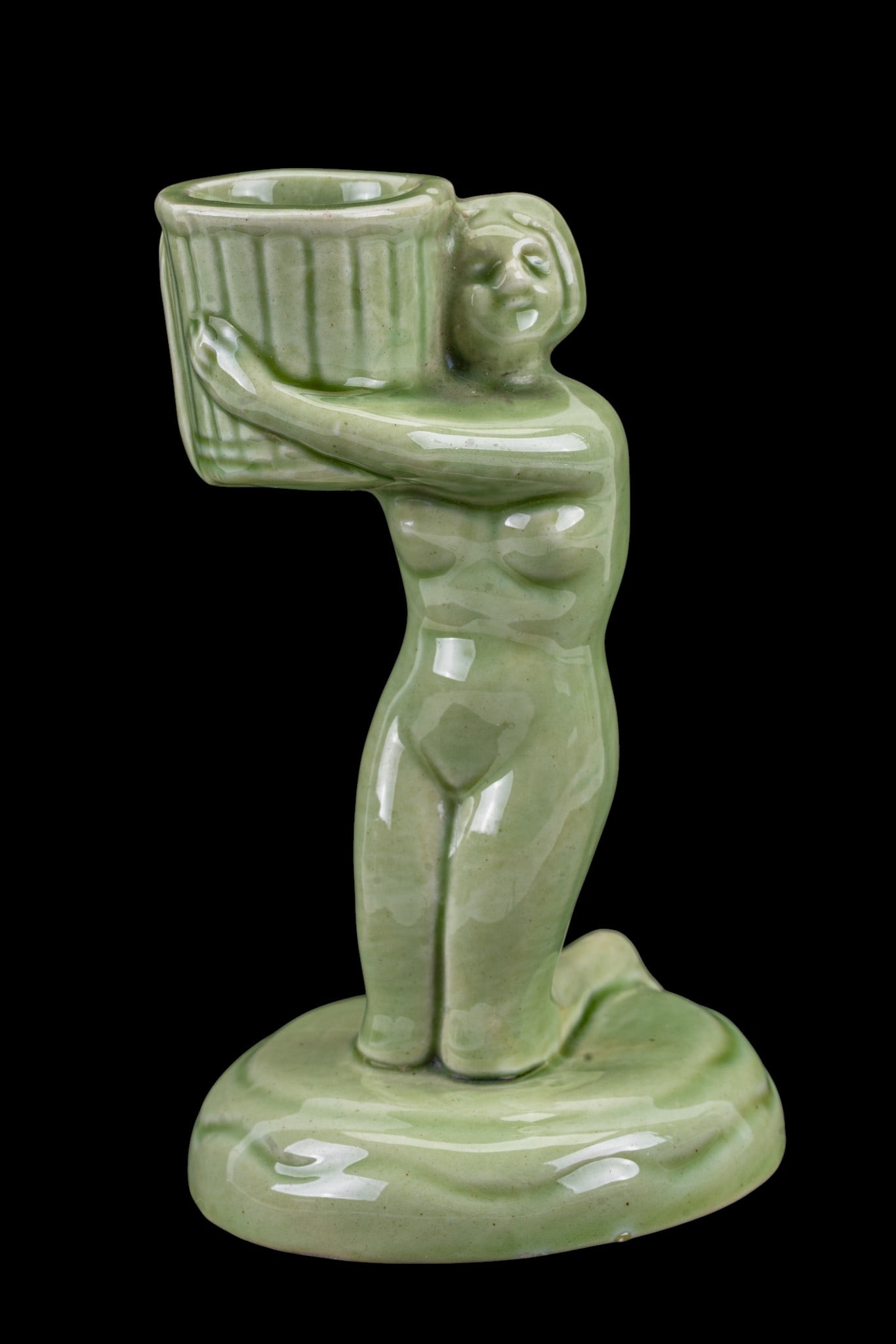Green Ceramic Figural Candle Holder: Green glazed ceramic candle holder measuring approximately 4.75 inches tall, featuring a stylized female figure supporting a cylindrical cup. The piece is molded in one form and finished with an even