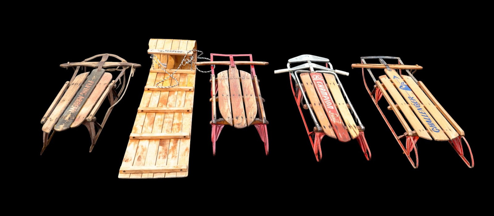 Sleds (4) and Torpedo Toboggan: Four rail sleds featuring various wood and metal designs by Champion, Flying Arrow, and Challenger, along with one wooden toboggan sled marked 'TORPEDO.' All pieces are constructed from wood with meta