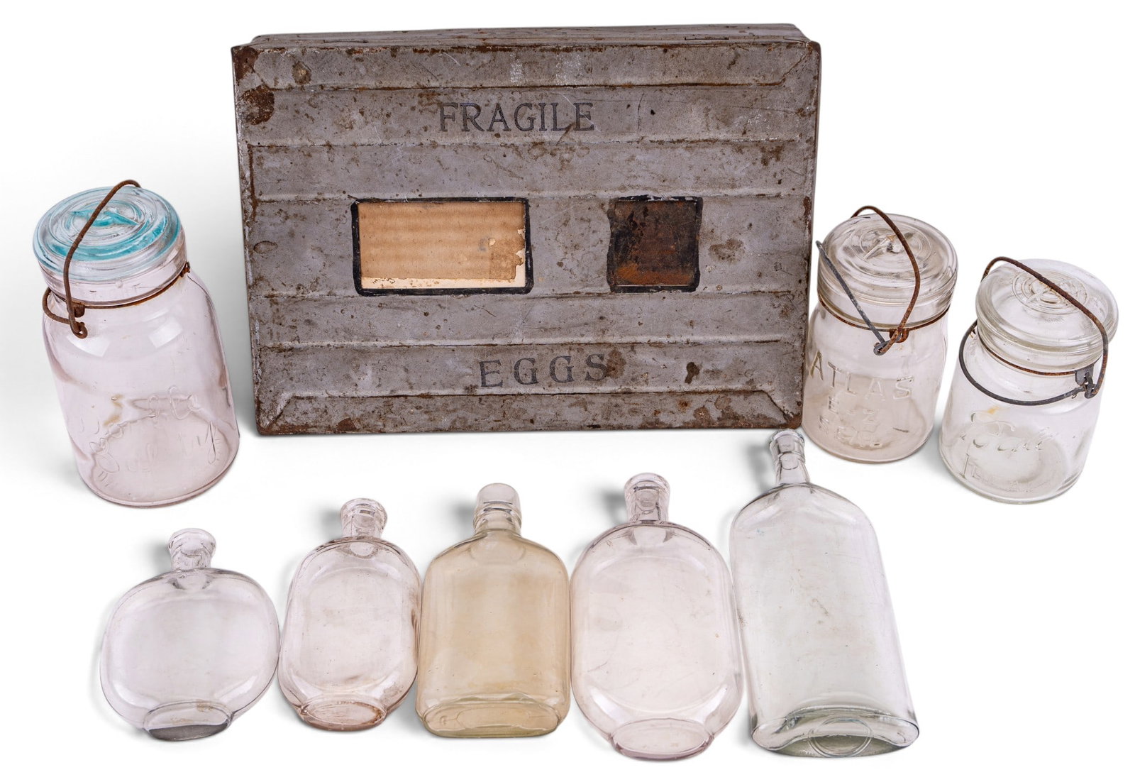 Vintage Metal Egg Crate, Ball Jars, Glass Bottles: One metal egg crate marked for 2 dozen eggs from Hochschild, Kohn & Co., three Ball-branded glass jars with glass lids and metal bails, and five vintage flat glass bottles of various shapes and sizes.