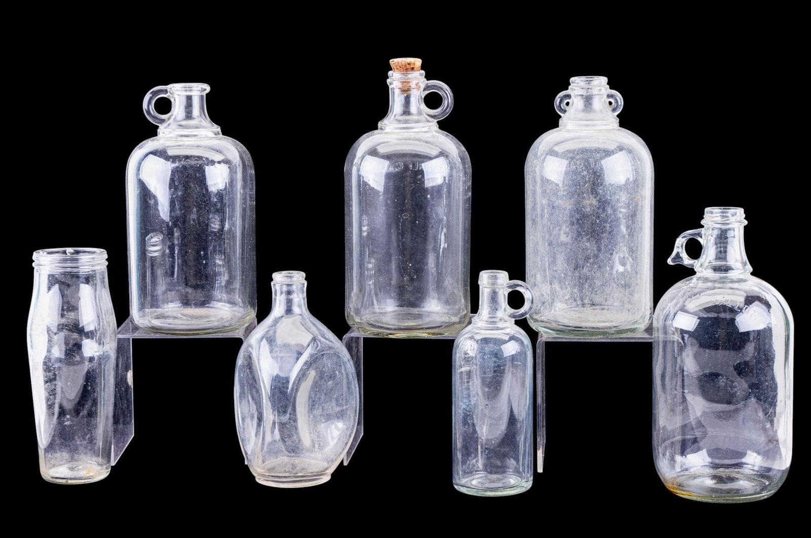 Vintage Glass Bottles & Jugs (7pcs, Assorted): Seven clear glass bottles and jugs: four marked "ONE HALF GALLON" with loop handles, one milk bottle, one triangular liquor flask marked with federal message and "Haig & Haig Ltd Edinburgh Scotland,"