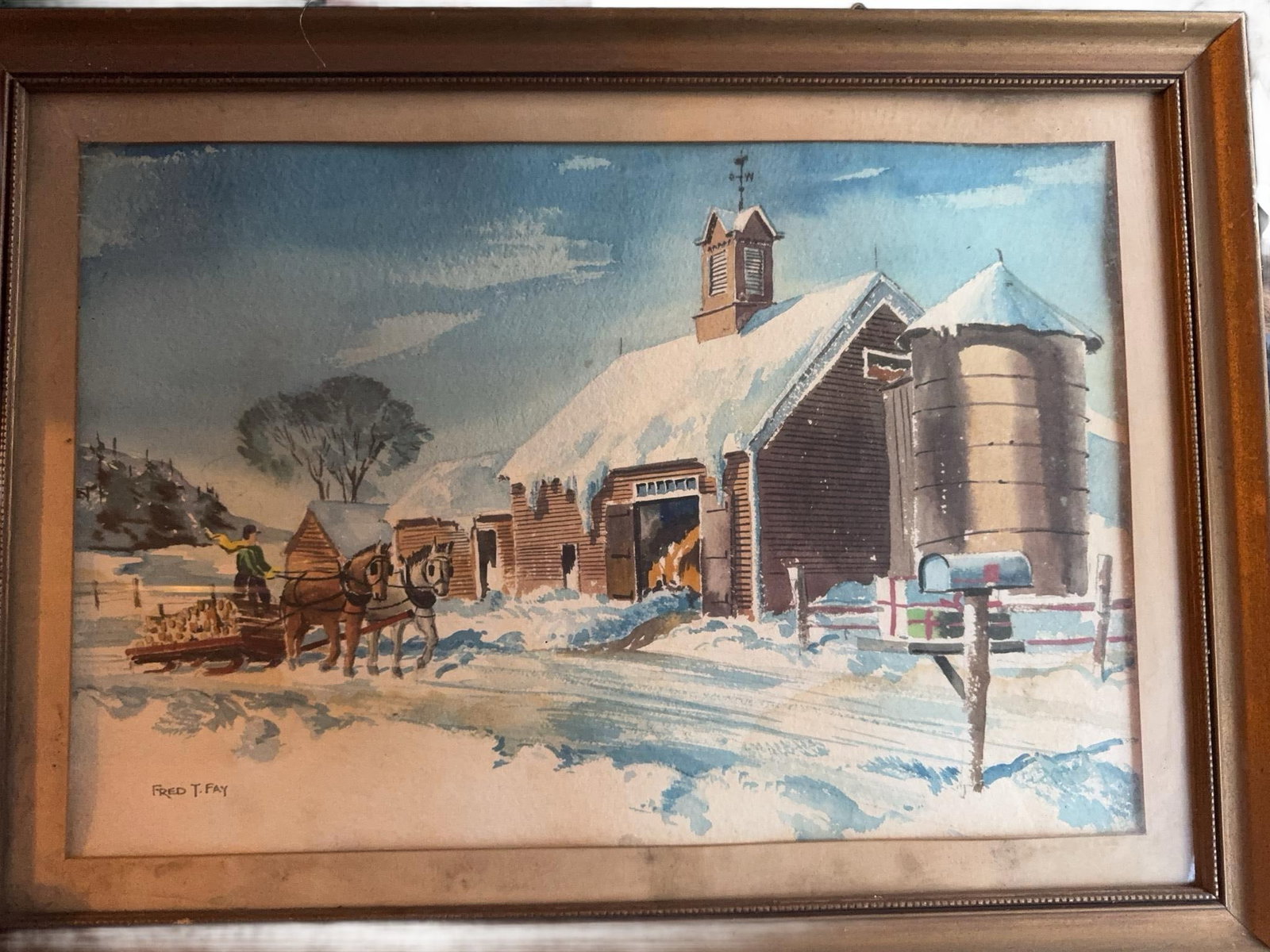 Fred T. Fay Watercolor Winter Barn Scene: Watercolor painting by Fred T. Fay depicting a rural winter scene with a barn, silo, horse-drawn wagon, snow-covered landscape, and mailbox, presented in a wooden frame with glass. Artist signature vi