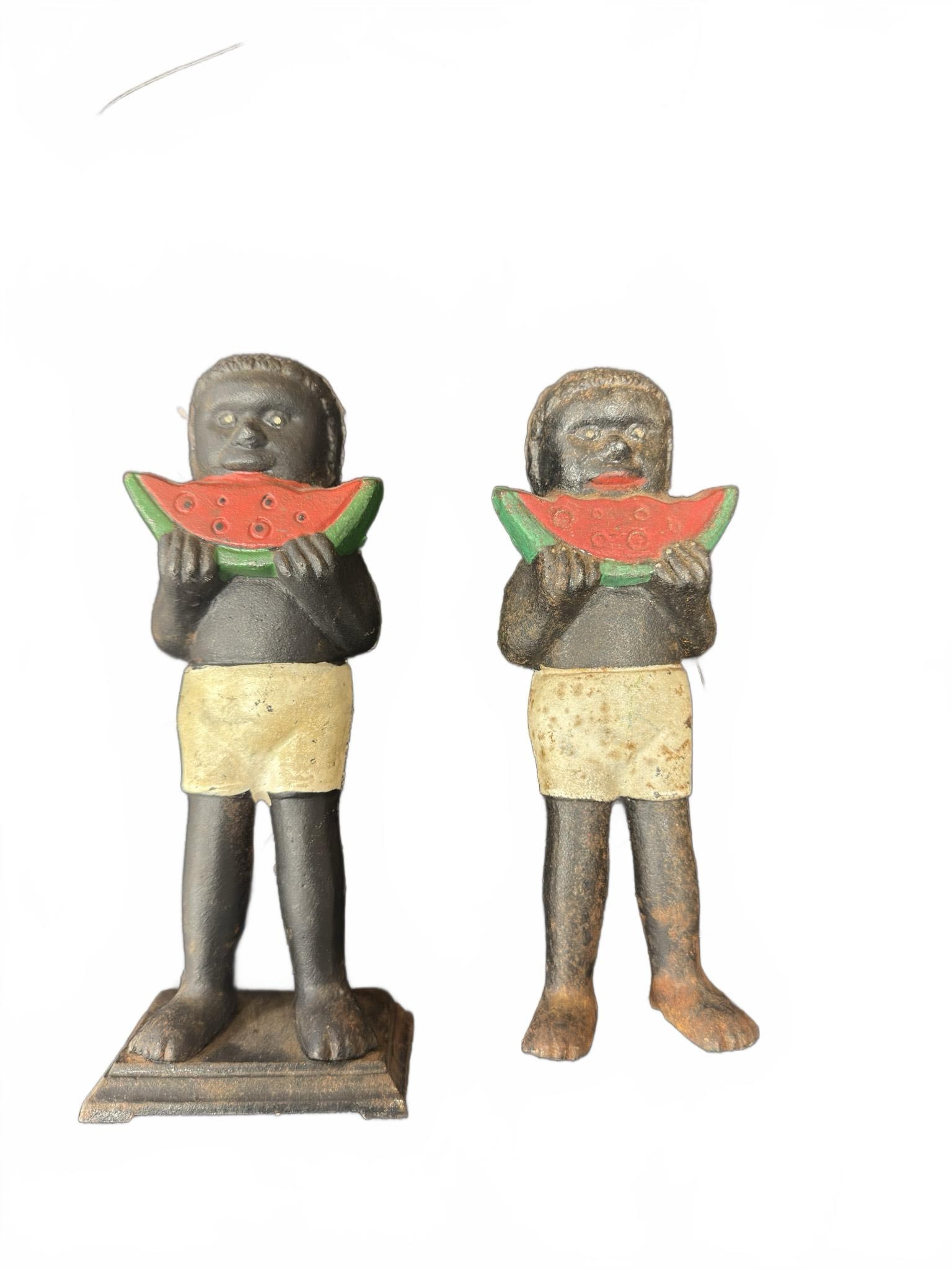 Cast Iron Watermelon Coin Banks: Two cast iron coin banks featuring figures holding watermelon slices. One bank includes its base and is missing the screw for the backplate, while the other bank is missing the base. Both display pain