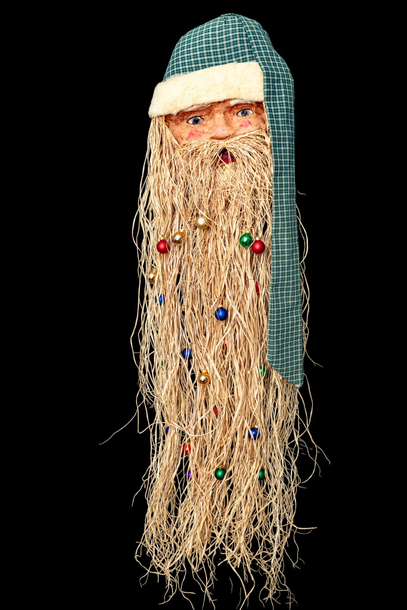 Handmade Folk Art Santa Hanging: Vintage "Old World" style papier-mache Santa Claus wall hanging featuring a hand-painted face, a long natural raffia straw beard embedded with miniature ball ornaments, and a green plaid stocking cap 