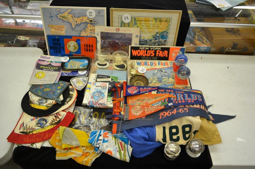 1964 New York Worlds Fair Grouping: 1964 New York Worlds Fair grouping includes; seven pennants of various sizes, four hats, three hankies, an oven mitt, a tablecloth (some stains) a license plate, a decorative license plate, and a 100%