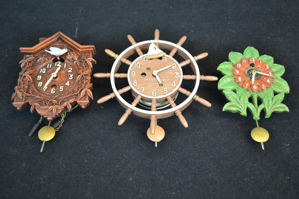 Lux and Westclox Grouping: Three clocks include; a Lux Sunflower Pendulette, featuring a red face with green leaves (some loss to stems), a Lux Swinging Bird Pendulette, and a Westclox Ships' Wheel clock in red and white; large