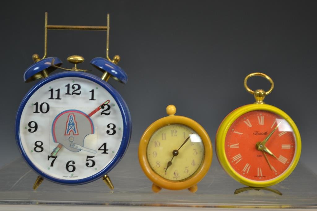 West German Forestville Alarm Clock and Two Others: Three alarm clocks; an orange and yellow tin travel alarm by Forestville marked "West Germany", a small alarm clock marked "German" in what appears to be a Bakelite case, and a third marked "West Germ