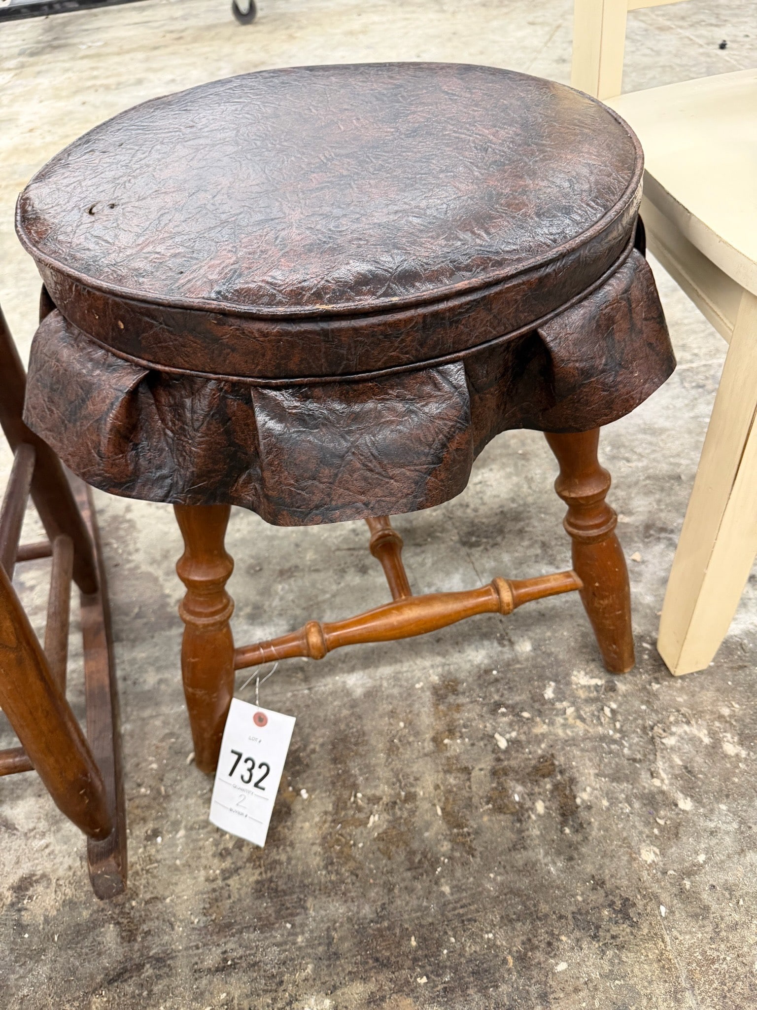 Wooden Stool with Leather Upholstered Seat: A wooden stool featuring turned legs and a ruffled, brown leather upholstered seat. The frame showcases a natural wood tone with a cross brace for added stability.