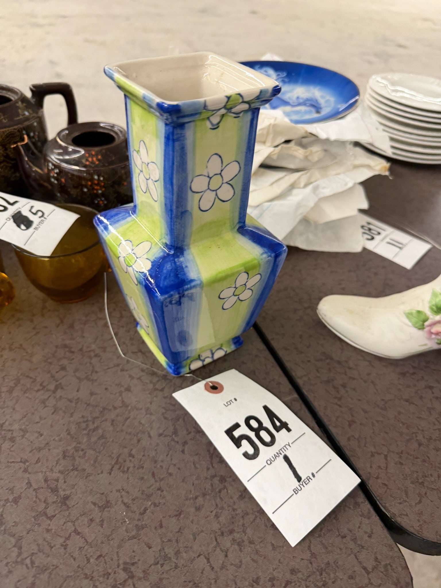 Square Ceramic Vase with Floral Design: Square-shaped ceramic vase featuring a hand-painted floral design on a vibrant lime green and blue background. The vase has a modern geometric form with delicate white flowers accentuating its surface