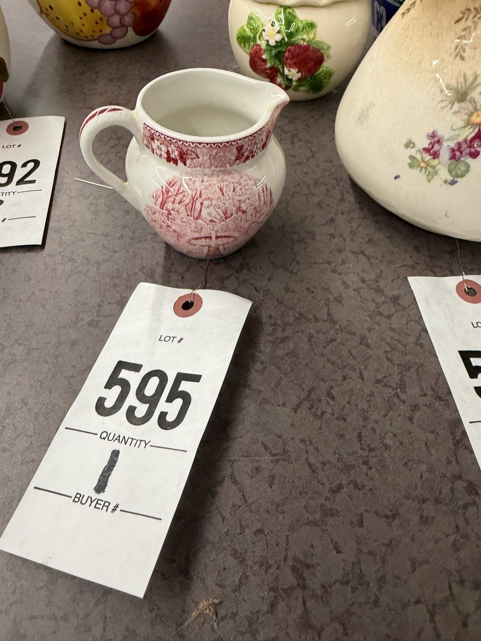 Red Transferware Ceramic Pitcher with Handle: Red transferware ceramic pitcher featuring a classic handle design. Decorated with intricate patterns in hues of red, it is ideal for display or functional use.
