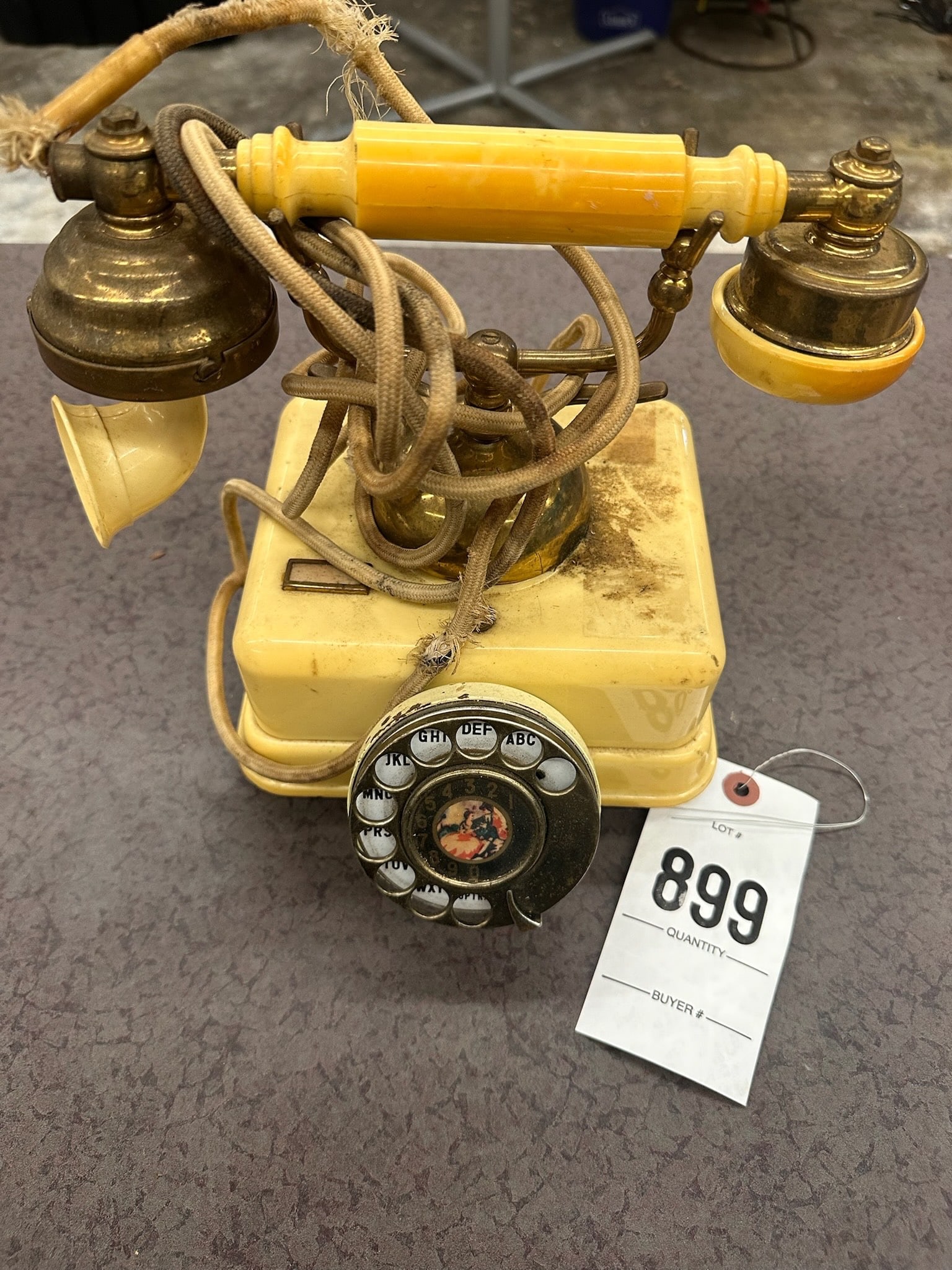 Vintage Rotary Dial Telephone with Brass Accents: Rotary dial telephone featuring a plastic body in a yellow finish complemented by brass accents. Includes a cloth-covered cord and a rotary dial with detailed numbers.