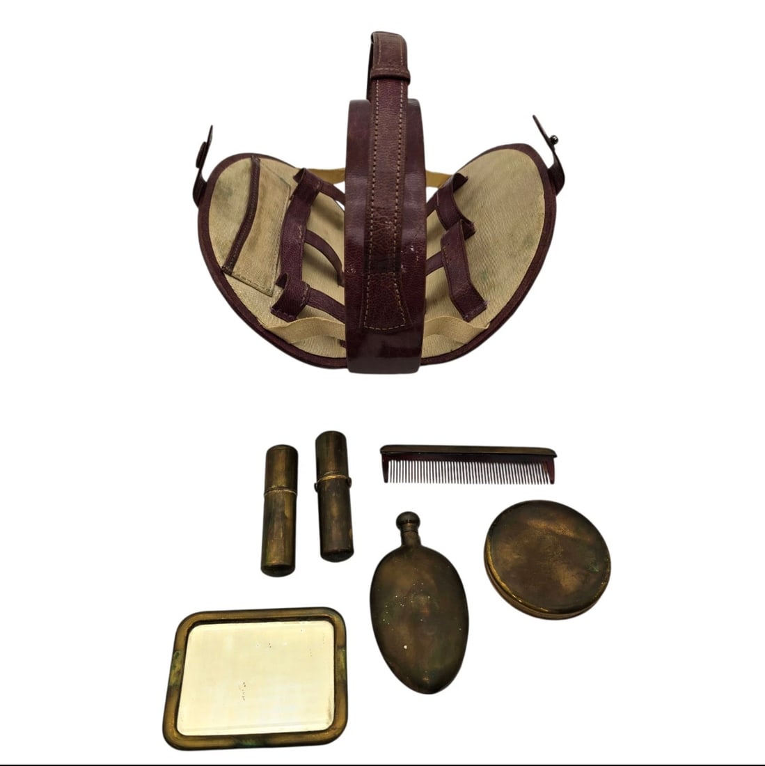 Vtg Travel Make Up Kit Travel Bag Wtih Adjustable Handle: A vintage or antique travel vanity kit featuring a unique folding burgundy leather carry basket with straps. It includes a matching set of aged brass vanity accessories: a hand mirror, a hairbrush, a 