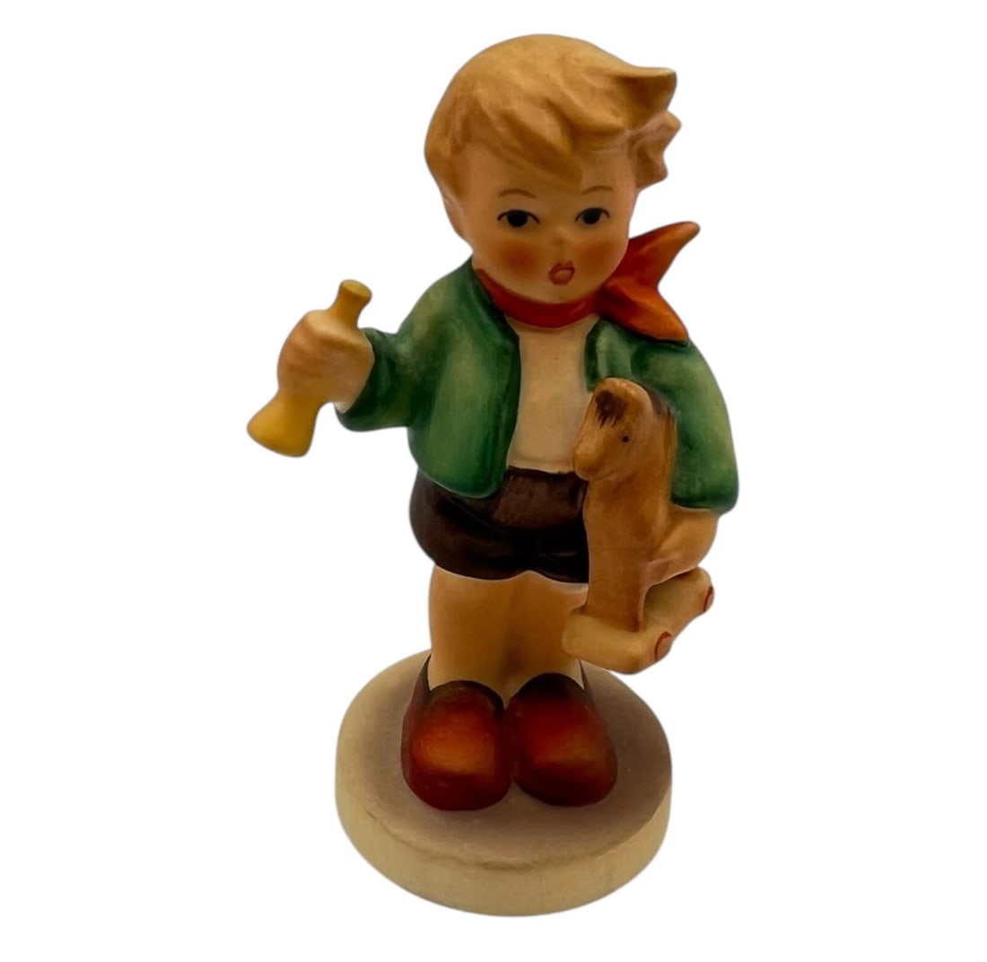 Goebel MI Hummel Figurine Boy with Toy Horse And Trumpet 3.5" Tall: vintage Goebel Hummel porcelain figurine featuring a young boy ready for playtime. He wears a green jacket, brown shorts, and a red neckerchief, while cradling a small wooden wheeled toy horse under o