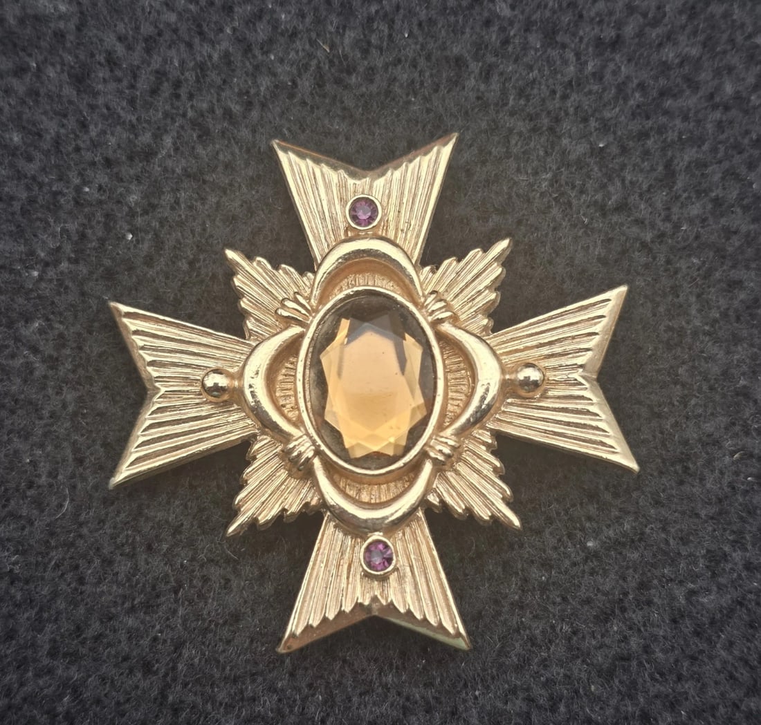 Vintage Avon Alegro Gold Tone Topaz Rhinestone Maltese Cross Brooch Pendant: A striking vintage gold-tone Maltese cross statement pin. The center features a large, faceted oval amber-colored glass rhinestone, flanked on the vertical points by two small, brilliant purple chaton
