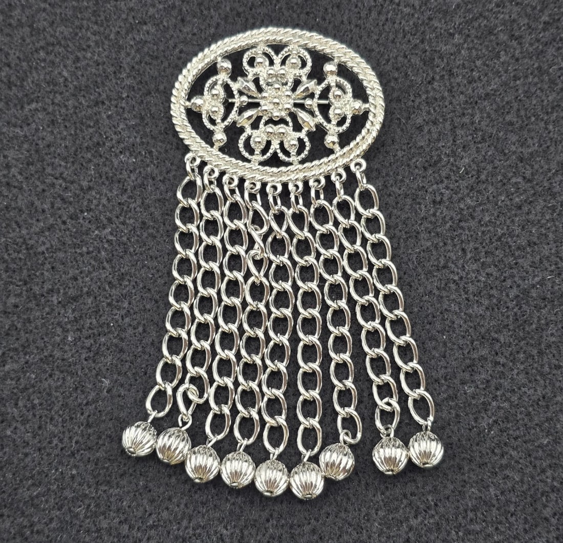 Vintage Sarah Cov Silver Tone Brooch with Dangling Chains & Filigree Detail: chatelaine-style tassel brooch. Features an oval openwork filigree top piece framed with a classic twisted rope border, suspending nine rows of fluid, hanging anchor link chains finished with decorati