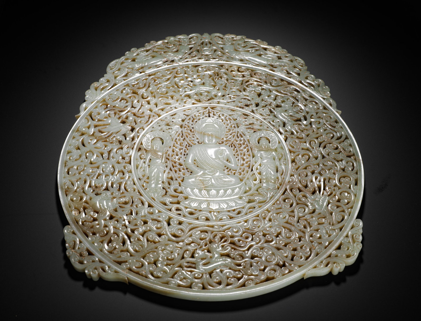 A ROUND PENDANT WITH THE PATTERN OF "BUDDHA" CARVED THROUGH HETIAN JADE IN THE MING DYNASTY: H:40.5cm (15.94in) W:34.5cm (13.58in) Weight:2840g (6.26lb)This is a Ming Dynasty Hetian jade round plaque, carved from smooth bluish-white jade with natural patina. The round plaque features a multi-
