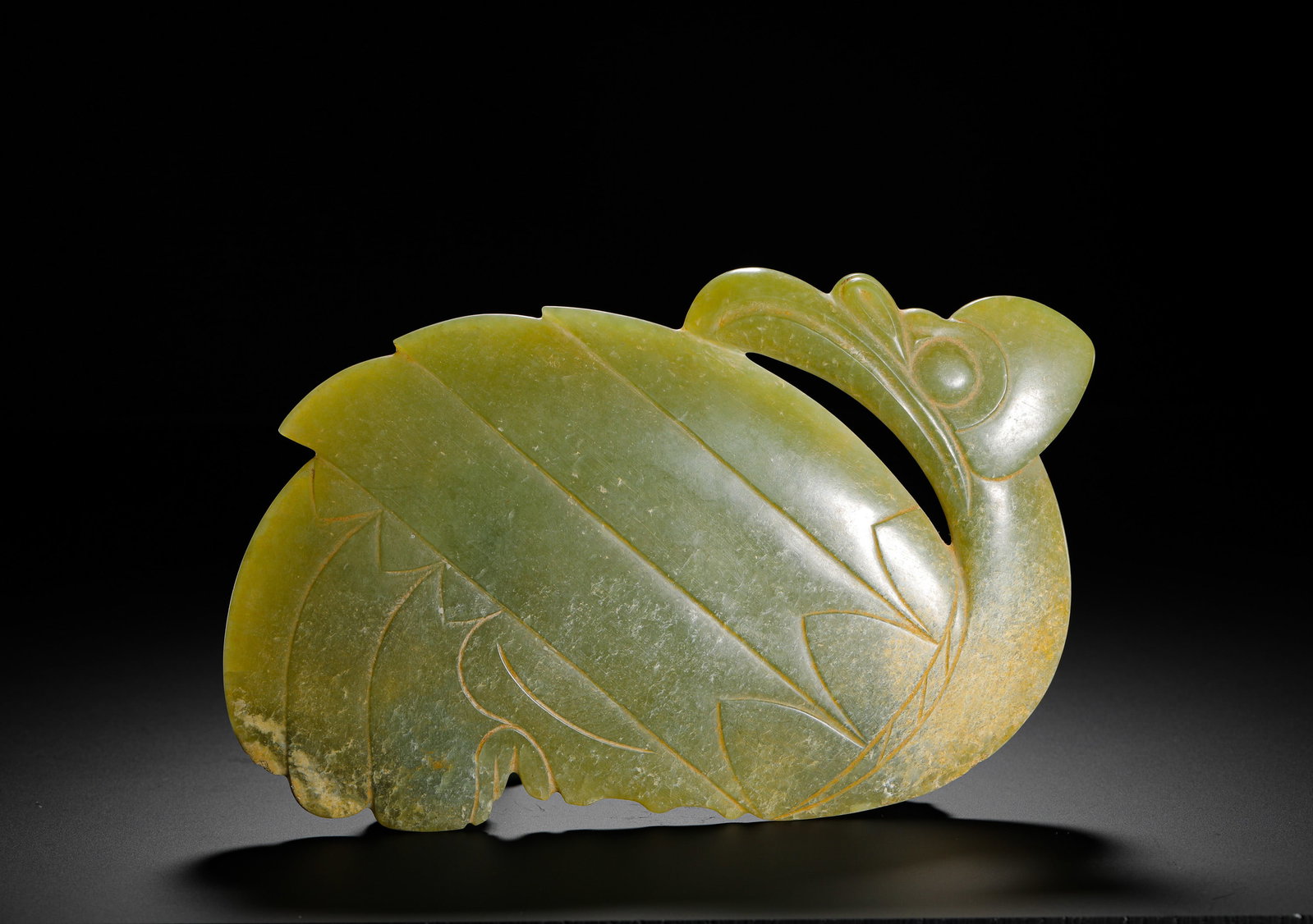 RED MOUNTAIN CULTURE GREENISH-YELLOW JADE PHOENIX PENDANT: H:12.5cmW:19cmWeight:410g Hongshan jade phoenix carved in coiled backward-looking form, simple incised lines depicting wing feathers, smooth jade with natural yellow patina, an ancient sacred bird rit