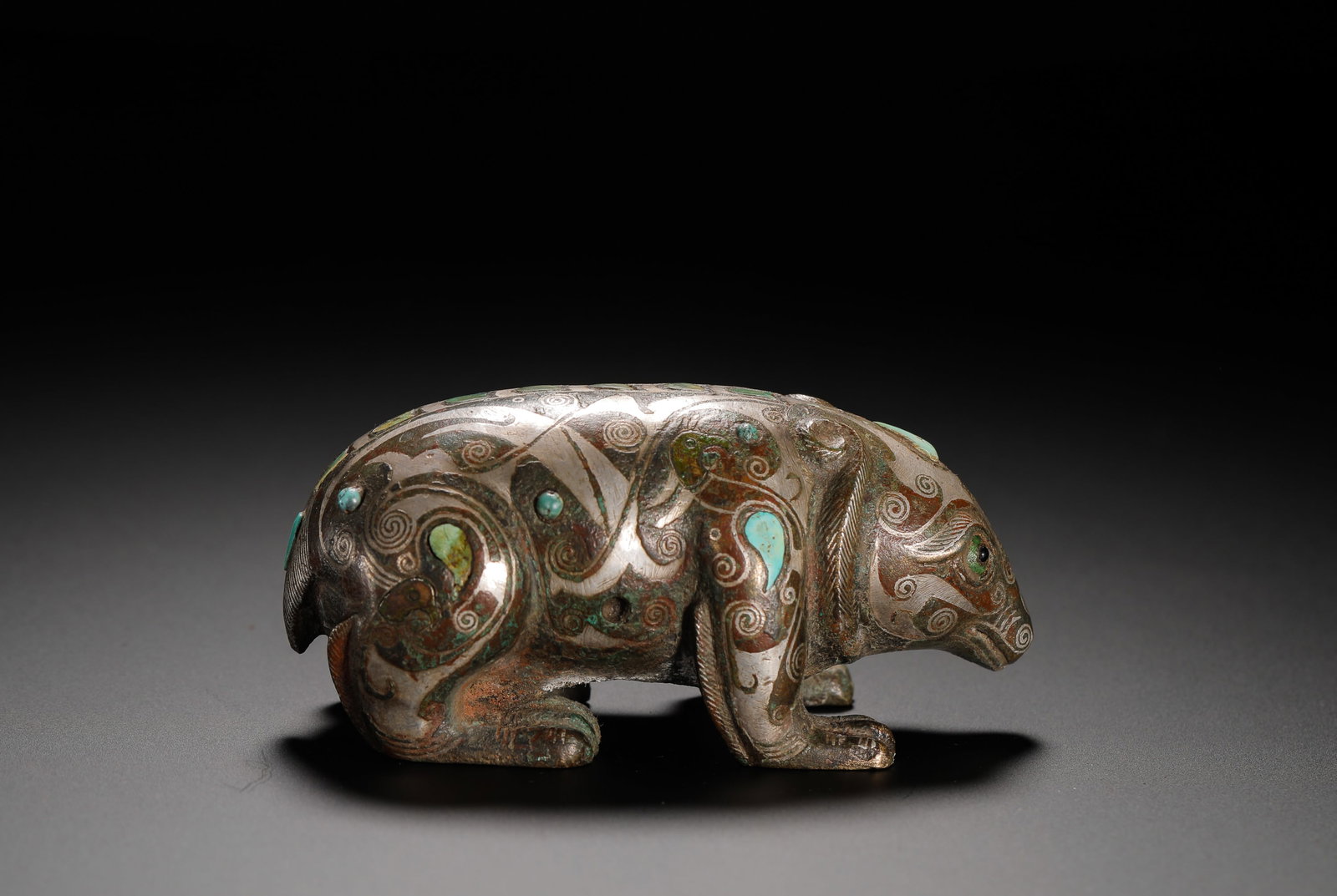 BRONZE INLAID WITH SILVER FROM THE HAN DYNASTY WITH TURQUOISE BEAR-SHAPED PEDESTAL: H:4cm(1.57in)W:9cm(3.54in)Weight:210g(0.46lb)These objects were used to hold down mats. The bear motif symbolized strength and good fortune, while the use of silver and turquoise inlay signified the o