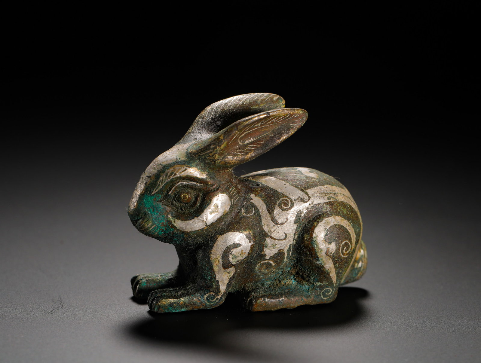 A HAN DYNASTY BRONZE RABBIT-SHAPED MAT WITH INLAID SILVER: H:6cm(2.36in)W:7.5cm(2.95in)Weight:180g(0.40lb)These objects were used to hold down mats. The rabbit motif symbolized good fortune and agility, while the use of silver inlay signified the owner's stat