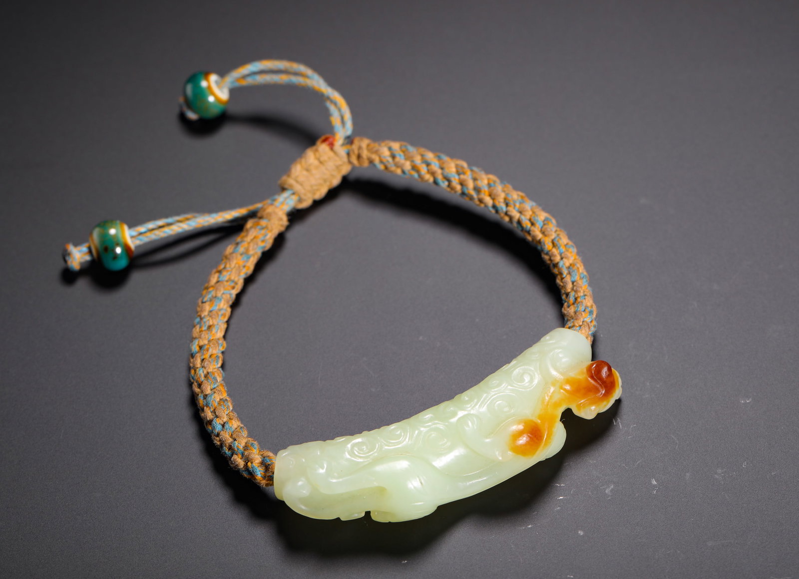 QING DYNASTY HETIAN JADE DRAGON-PATTERNED HAND TOKEN: H:2.2cm (0.87in) W:0.2cm (0.08in) Weight:30g (0.07lb)This is a Qing Dynasty Hetian jade hand bracelet with a chi dragon pattern, carved from smooth greenish-white jade with natural reddish-brown inclu