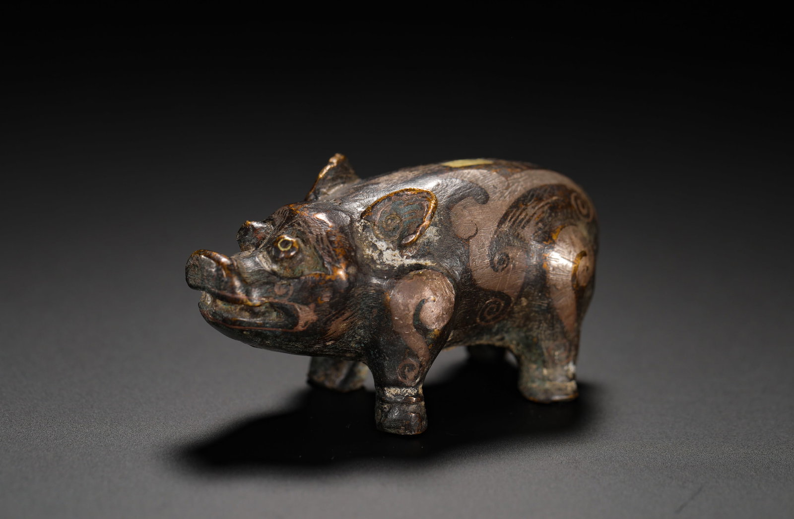 HAN DYNASTY BRONZE INLAID SILVER PIG-SHAPED CUSHION: H:3.3cm(1.30in)W:6cm(2.36in)Weight:90g(0.20lb)These objects were used to hold down mats. The pig motif symbolized prosperity and good fortune, while the use of silver inlay signified the owner's statu