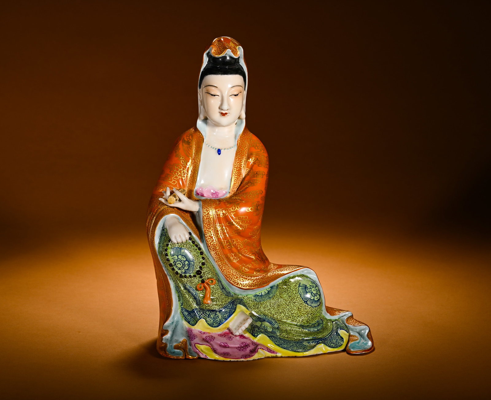 A SEATED STATUE OF GUANYIN IN BLUE AND RED WITH GOLD PAINTED IN THE QING DYNASTY: Height:28cm(11.02in)Width:18cm(7.09in)Weight:1680g(3.70lb)Famille rose porcelain statue of Zizai Guanyin with iron-red and gilt decoration. The Guanyin sits in relaxed casual posture, gentle serene fa