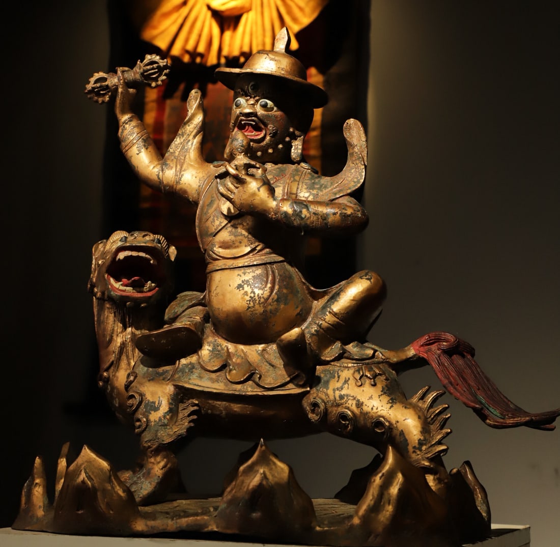A LION-RIDING GUARDIAN STATUE FROM THE QING DYNASTY: Weight:11150g.L:50cmH:49cmW:30cmThis is a Tibetan Buddhist gilt-bronze statue of the Dharma Protector Damchen riding a lion. Made of gilt bronze, the protector has a fierce face with three eyes, ridin