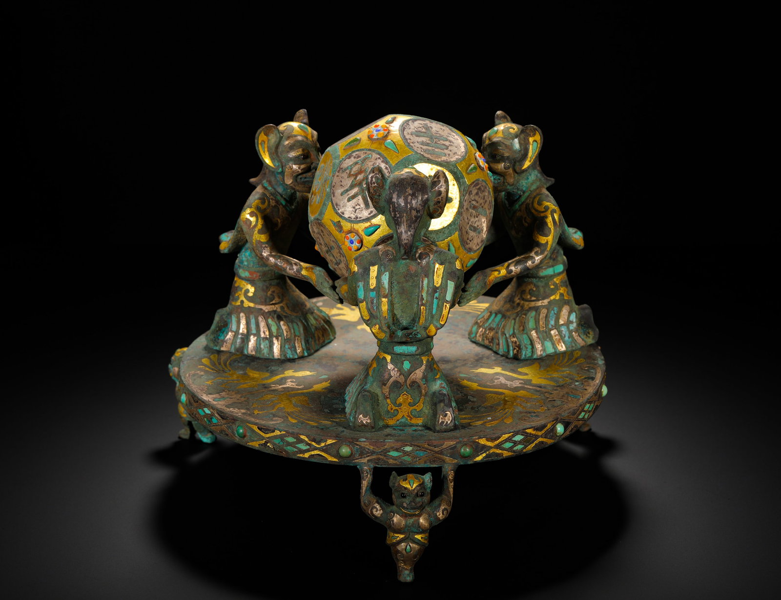 A TWELVE-SIDED BRONZE DICE WITH INLAID GOLD AND SILVER AND TURQUOISE FROM THE WARRING STATES PERIOD: Height:21cm(8.27in) Width:26cm(10.24in) Weight:3930g(8.66lb)Bronze ornament with a twelve-sided divination dice inlaid with gold, silver and turquoise. The round tray has three beast-shaped feet, with