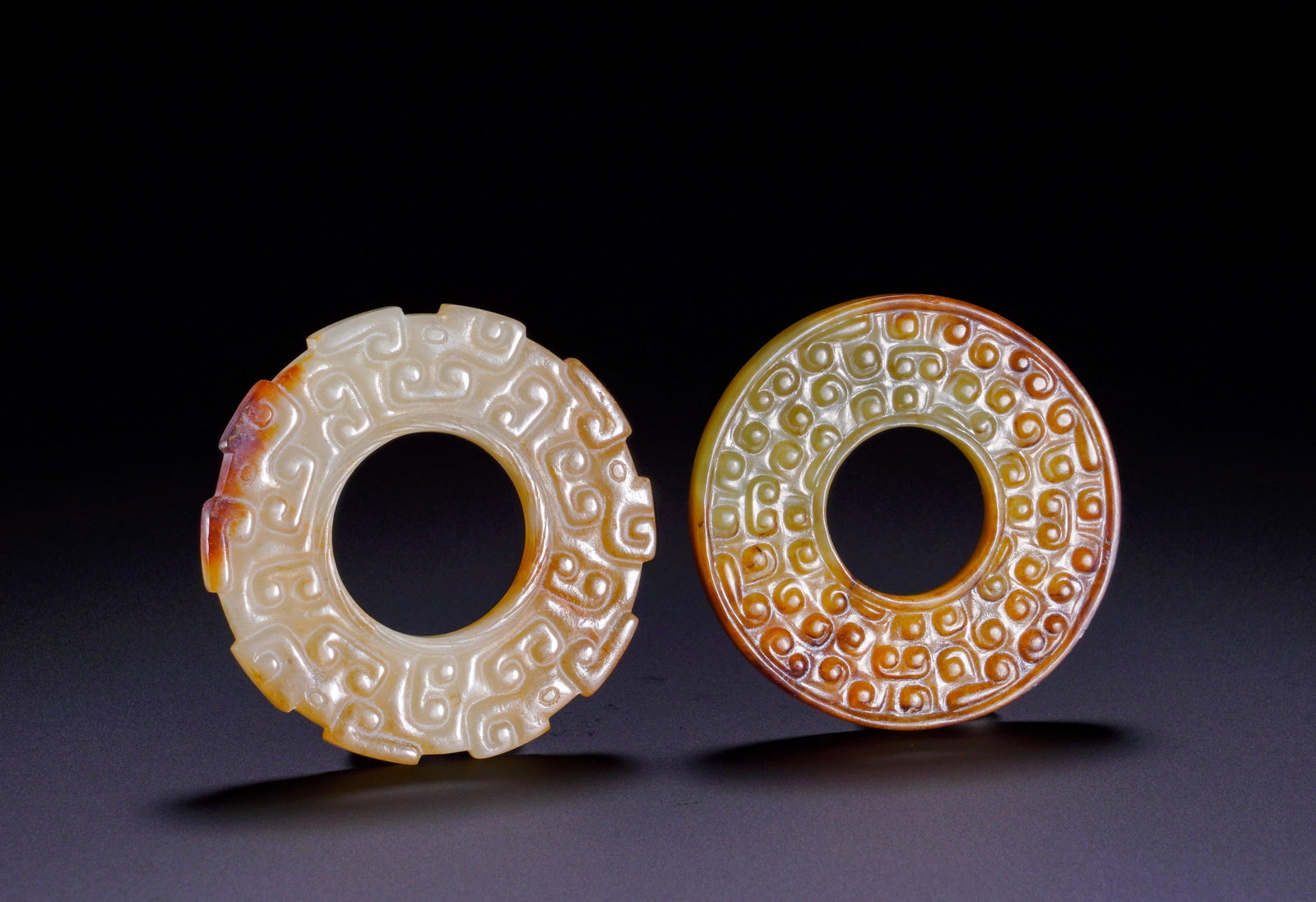 A SET OF TWO HAN DYNASTY JADE RINGS: Diameter:4.8cm(1.89in)Weight:40g(0.09lb)Set of two jade rings of Han Dynasty.The left white jade ring is covered with natural yellow and red patina, decorated with symmetrical dragon heads and continu