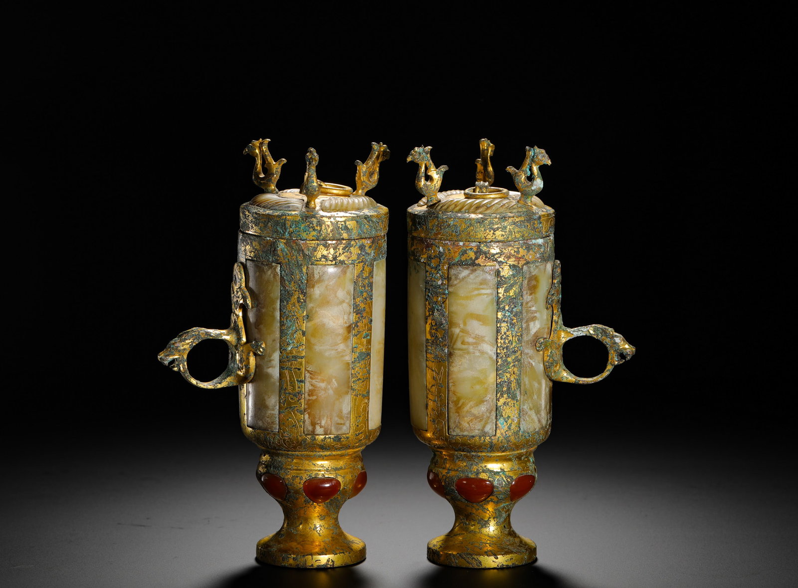HAN DYNASTY BRONZE GILDED CUP WITH JADE EAR AND HIGH FOOT: Height:18cm(7.09in) Width:10cm(3.94in) Weight:1710g(3.77lb)A pair of Han Dynasty gilded bronze stem cups inlaid with white jade and red gemstones, dragon-phoenix shaped handles and three divine birds 