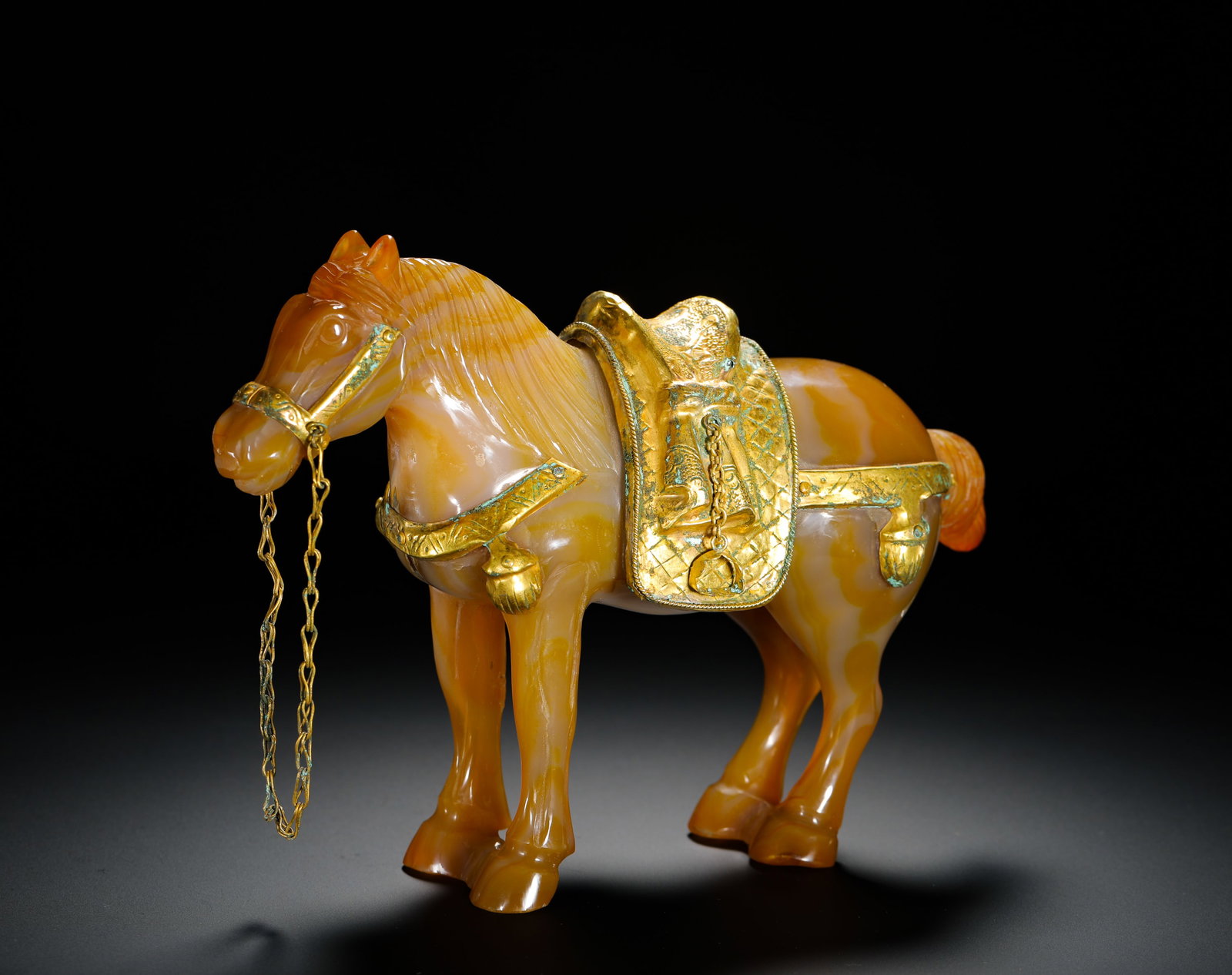 QING DYNASTY SILK AGATE GOLD-ENCRUSTED HORSE: Height:14cm(5.51in) Width:20.5cm(8.07in) Weight:1020g(2.25lb)Qing Dynasty agate standing horse statue decorated with full gilt saddle and reins. Solid whole agate carving with natural orange-white ban