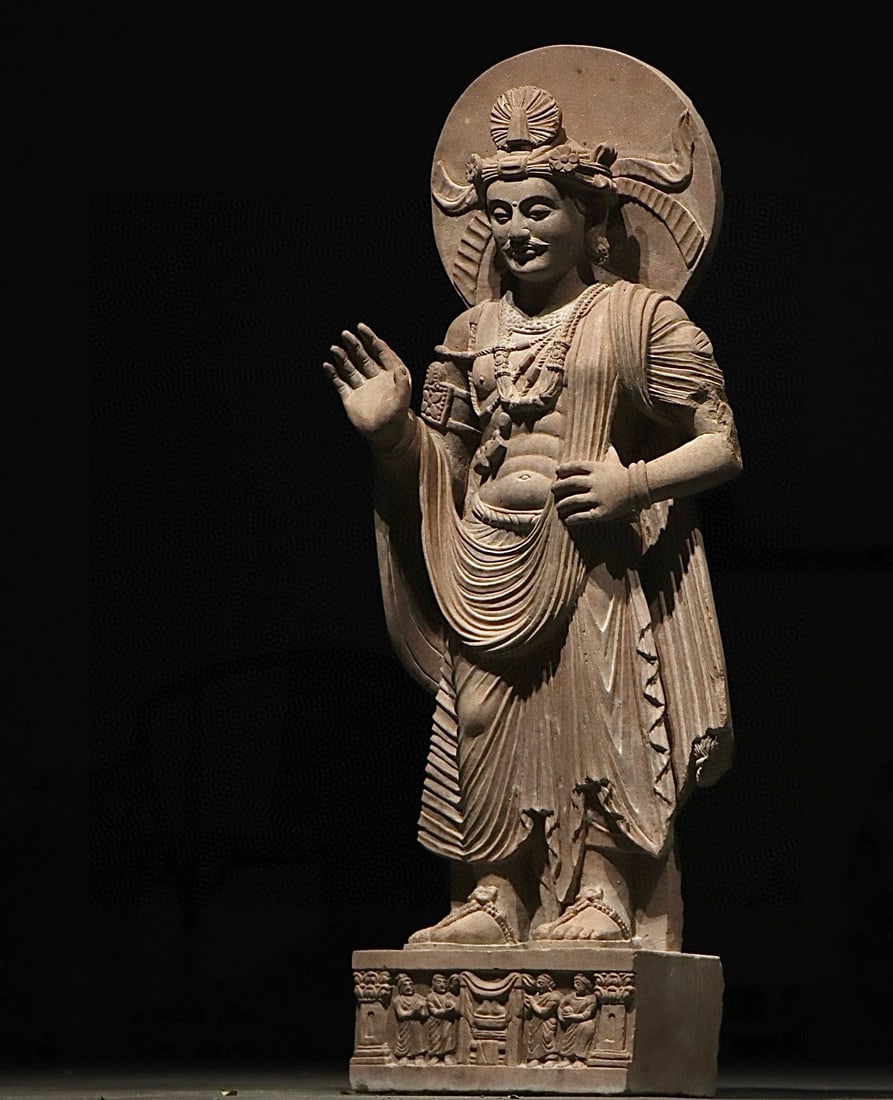 GANDHARA STATUES FROM THE 3RD CENTURY: H:116cm W:40cm T:26cmThis is a Gandhara-style stone standing statue of a Bodhisattva, crowned and draped in jewelry, with a halo behind. Its right hand forms Abhaya Mudra, with Greek-style wavy robe f