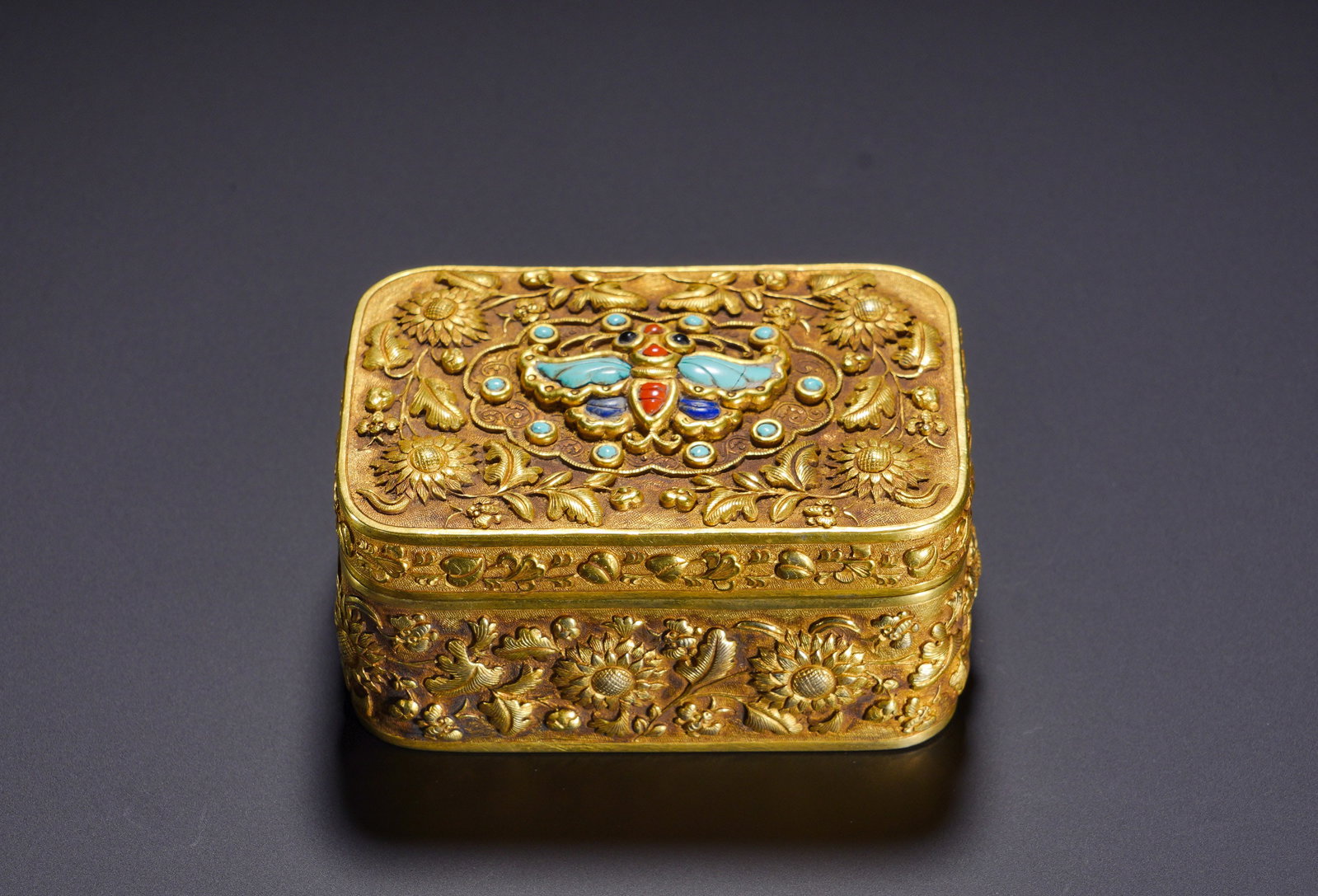 A Tang Dynasty silver-gilt embossed flower-butterfly inlaid treasure lid box: Height:4cm(1.57in), Width:8.2cm(3.23in), Weight:230g (0.507lb)Flower and butterfly patterns symbolise longevity and prosperity. Boxes of this kind were used to hold incense, jewellery or paste for imp
