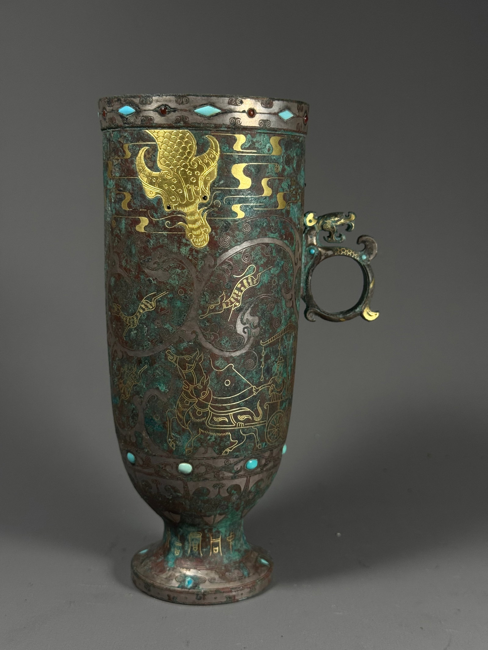 Han cuo gold inlaid turquoise hunting pattern single-eared high foot bronze cup: Height:17cm(6.69in), Width:9cm(3.54in), Weight:502g (1.107lb)Han Dynasty Bronze Stemmed Cup with Single Handle, Gold Inlaid Hunting Scenes and Turquoise InlayTall straight-bodied bronze wine vessel wi