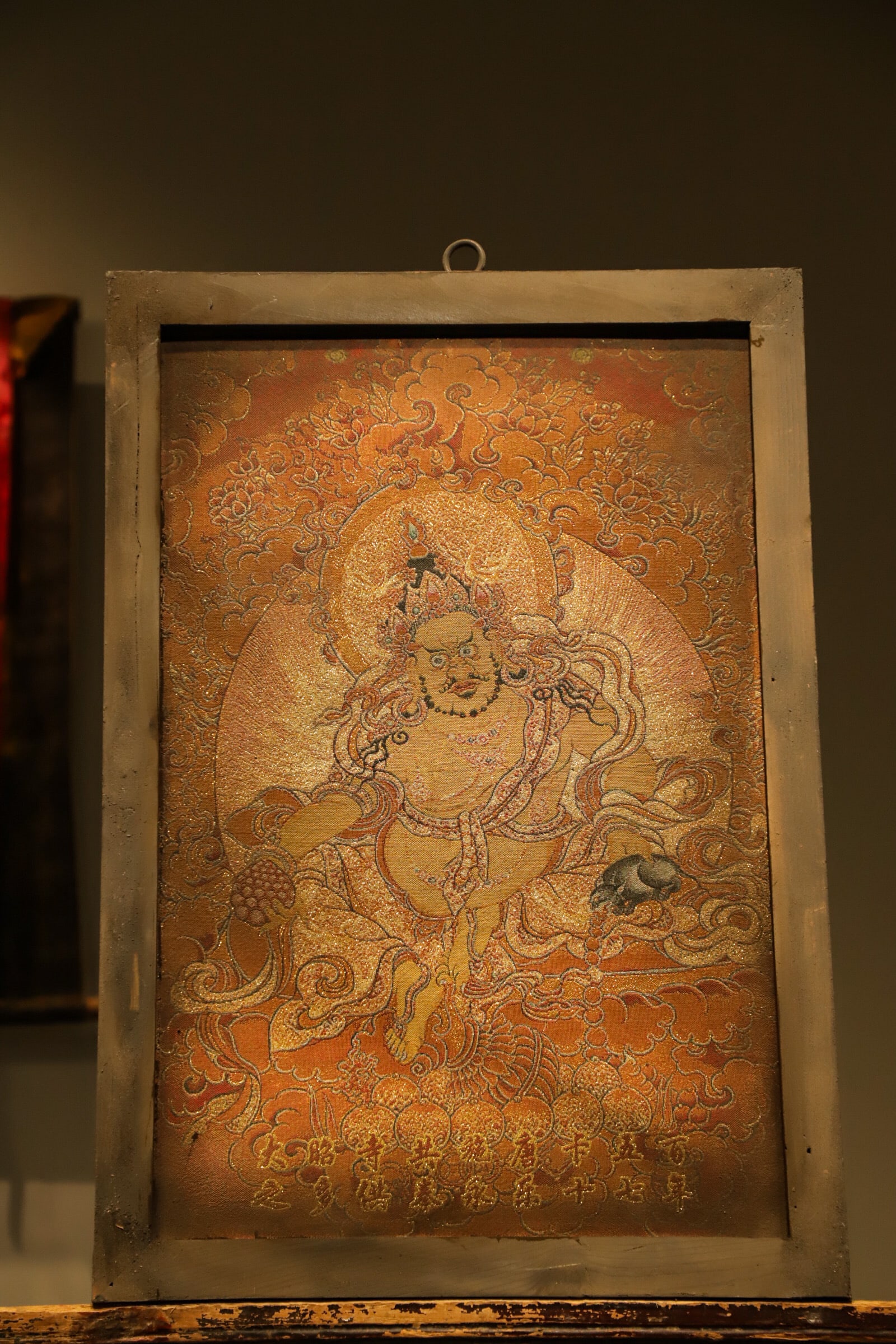 An old Thangka made of silk from the Qing Dynasty - a statue of the Yellow God of Wealth: Height:65cm(25.59in), Long:46cm(18.11in)Set in vintage wooden frame and woven with exquisite brocade craft. The Yellow Jambhala is golden in complexion, adorned with precious crown. He holds a wish-gr