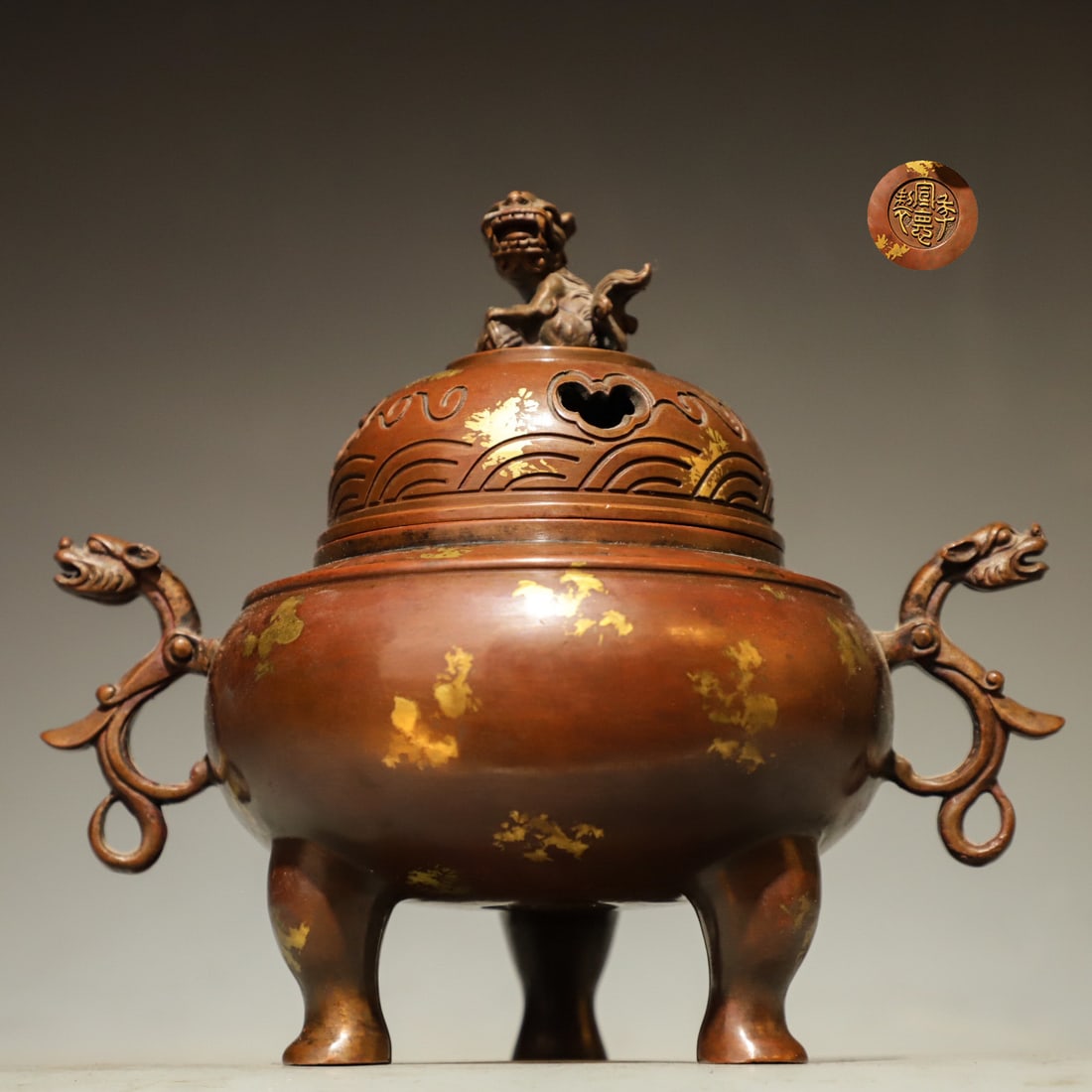 A three-legged incense burner with auspicious beast chilong ears from the Ming Dynasty: Weight:1967g (4.336lb), Height:16cm(6.30in), Long:18cm(7.09in), Width:12cm(4.72in)Crafted from purple bronze dotted with gold patches. The cover is crowned by a mythical lion suanni finial, carved wit