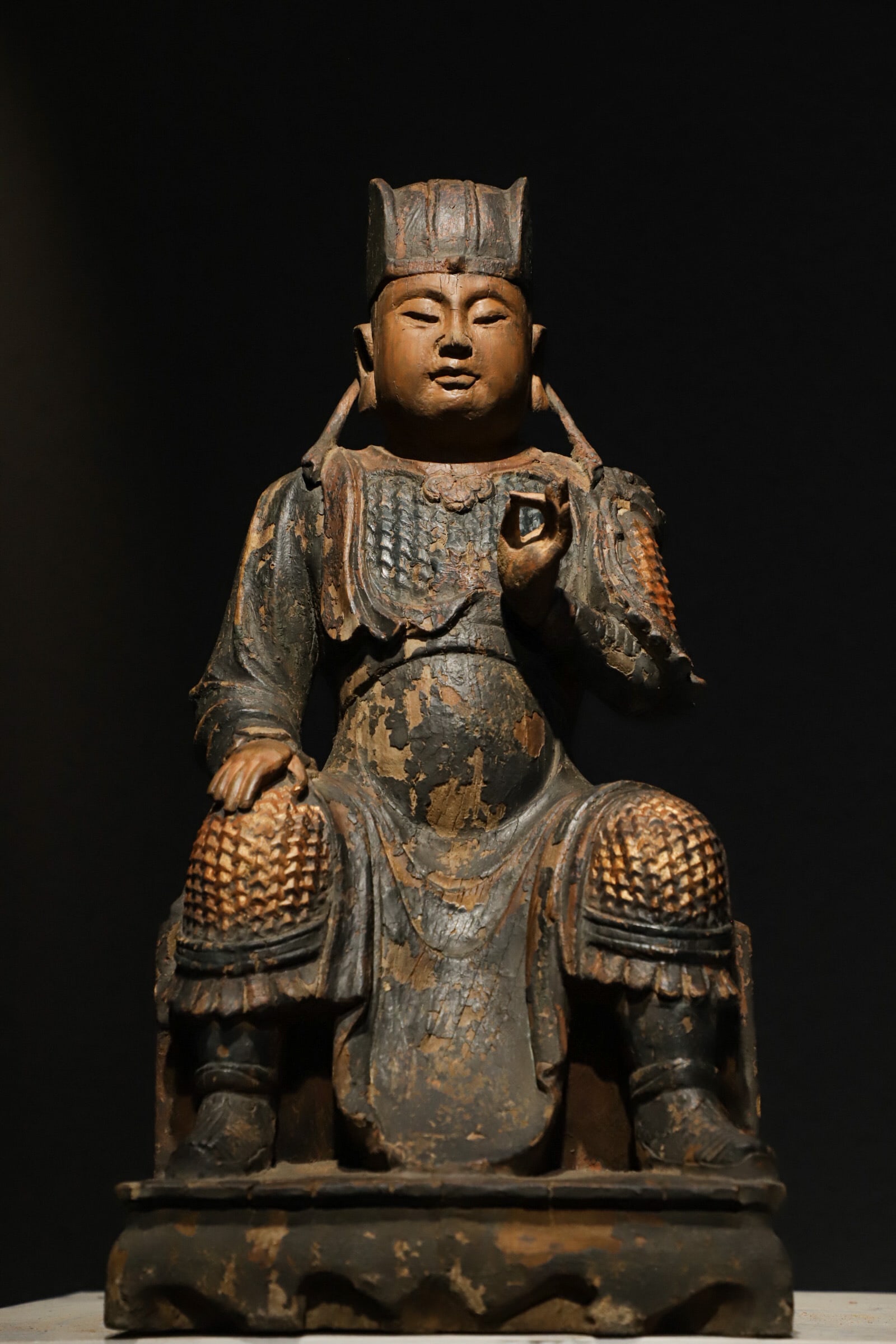 A sitting statue of a warlord in lacquer gold carved from wood from the Ming Dynasty: Height:42cm(16.54in), Long:21cm(8.27in), Width:21cm(8.27in)Carved from single wood, wearing military official hat with mild and serene facial features. Clad in scaled armor with original gilding, cove