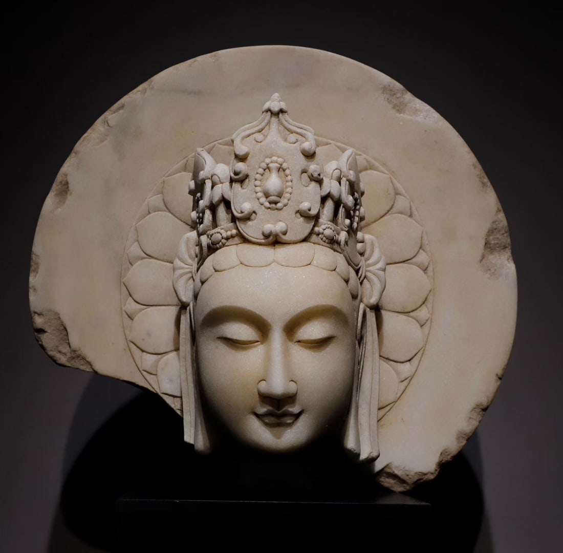 A white marble Bodhisattva head from the Northern Qi Dynasty: Height:42cm(16.54in), Width:48cm(18.90in), Thick:20cm(7.87in)White marble Bodhisattva head sculpture. The marble has fine, smooth texture. The elongated gentle face with closed eyes conveys serene