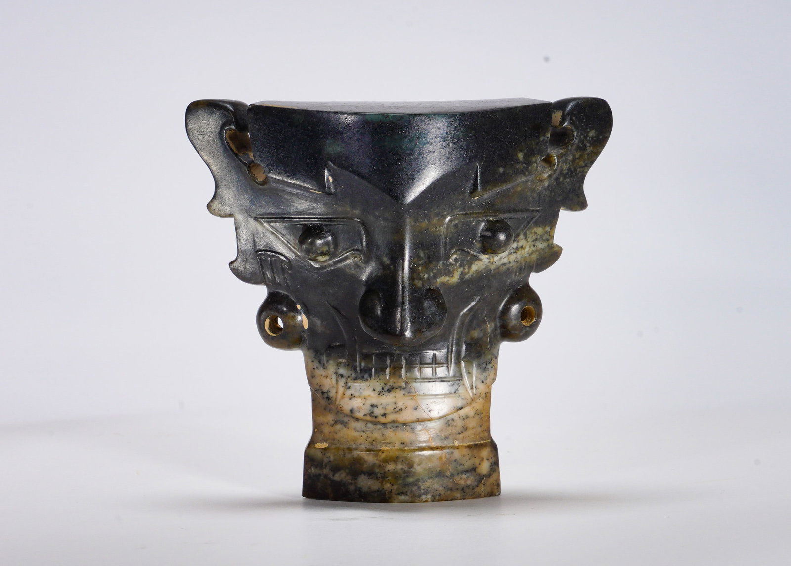 Shang Dynasty Hetian jade Divine Face: Height:9.5cm(3.74in) Width:11.5cm(4.53in) Weight:470g(1.04lb)The fully carved jade mask stands on cylindrical base, with protruding eyes, straight nose and lined teeth, wing-shaped ears with perforati