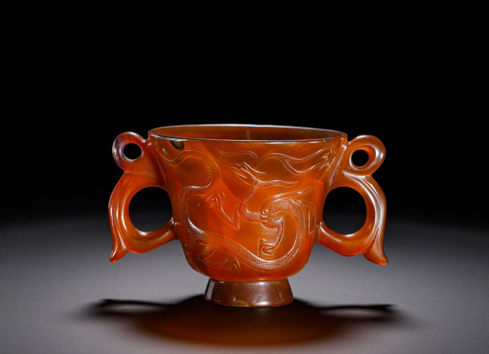 Liao Dynasty agate dragon pattern double-eared cup: Height:8cm(3.15in), Width:14cm(5.51in), Weight:300g (0.661lb)Agate Cup with Relief Dragon Pattern and Double HandlesCarved from a single piece of natural red agate with hollowed interior. It possesses