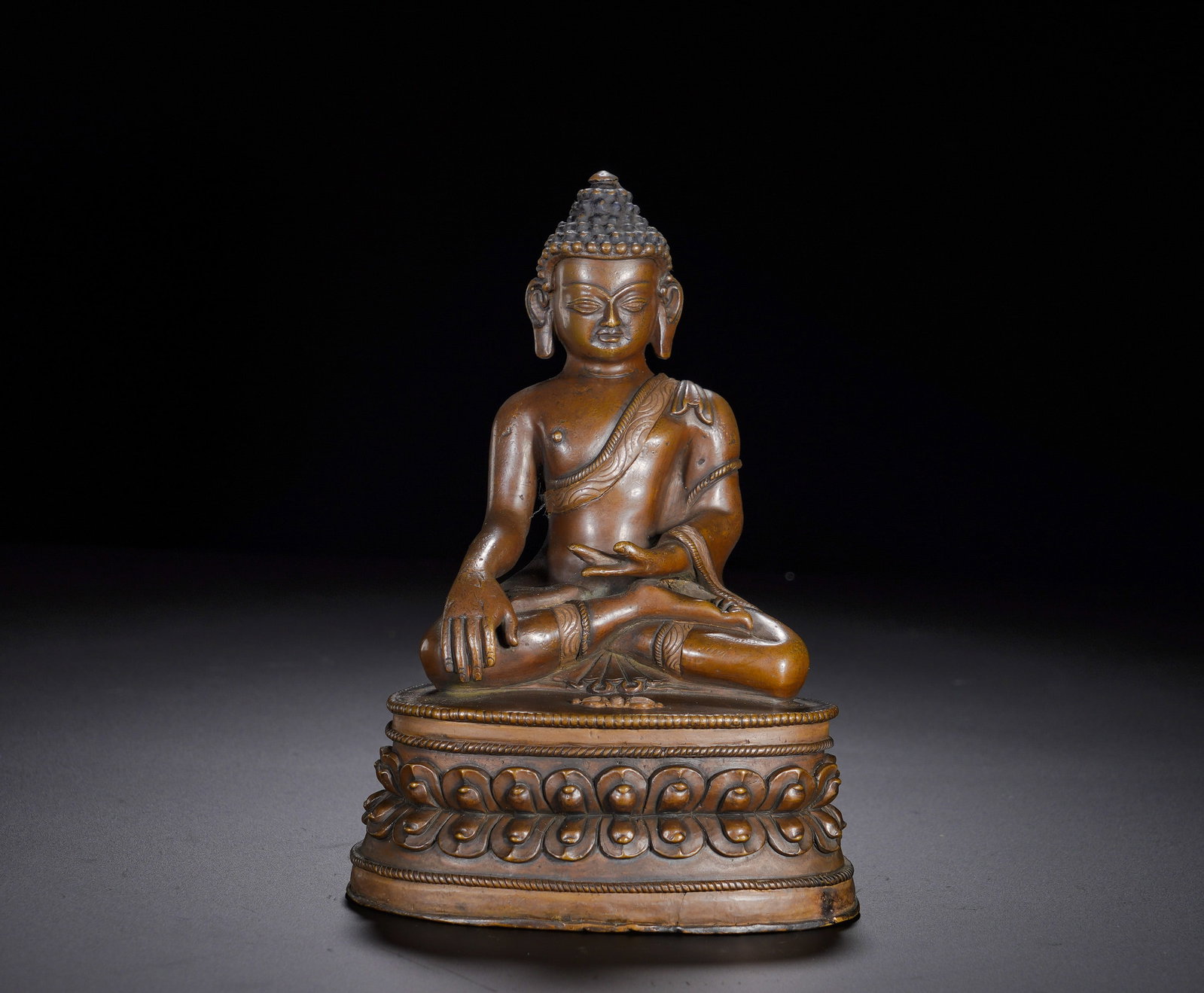 A red bronze statue of Sakyamuni attaining enlightenment from the Qing Dynasty: Height:15cm(5.91in), Width:10cm(3.94in), Weight:980g (2.161lb)This is a bronze seated statue of Shakyamuni Buddha, with Tibetan prayer inscriptions carved on the pedestal. The Buddha sits in full