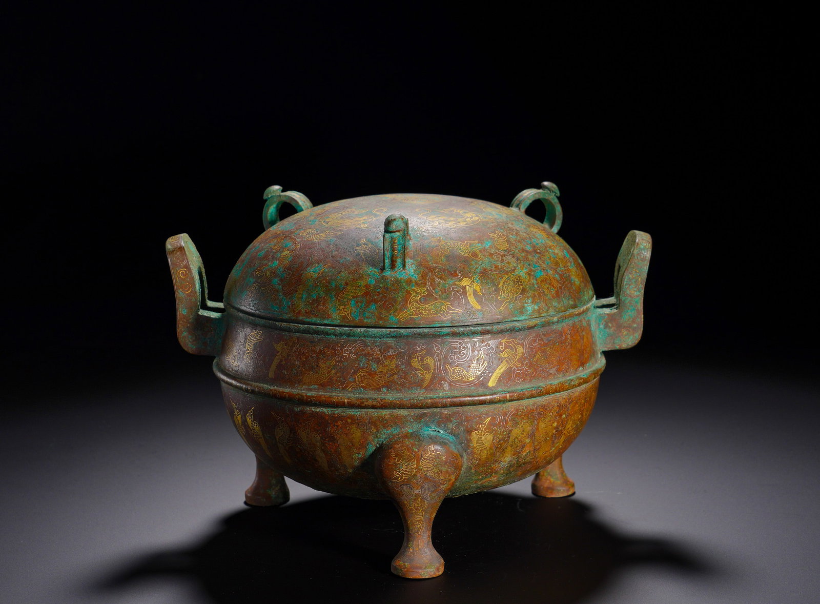 Bronze tripod with gilded auspicious beast patterns from the Warring States period: Height:15cm(5.91in), Width:22cm(8.66in), Weight:2620g (5.776lb)Cast bronze, spherical body surmounted by a domed lid. Symmetric upright flanges extend from the sides, supported by three beast-hoof fee