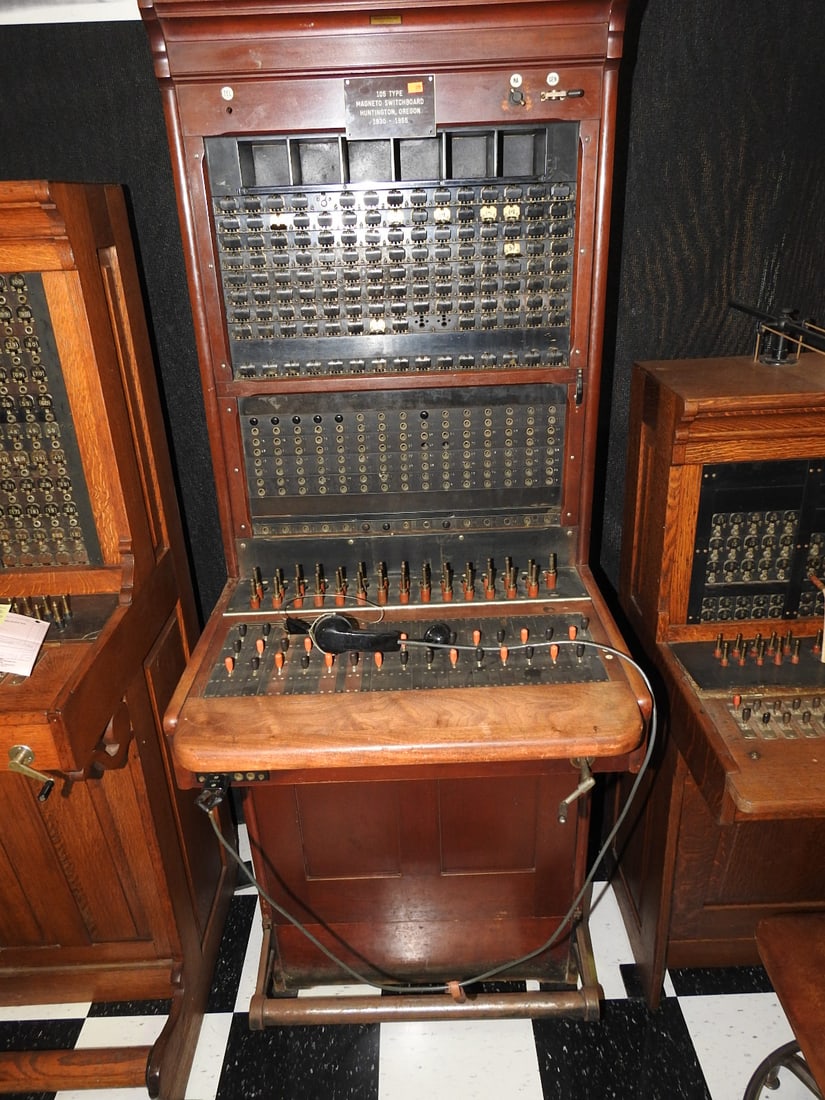 Western Electric 105 Type Magneto Switchboard: Large antique wooden 105 Type magneto switchboard with plaque reading Huntington, Oregon 1930-1955 and Western Electric label. Includes cord field, switches, plugs, receiver, and cabinet. Approx. 70 x