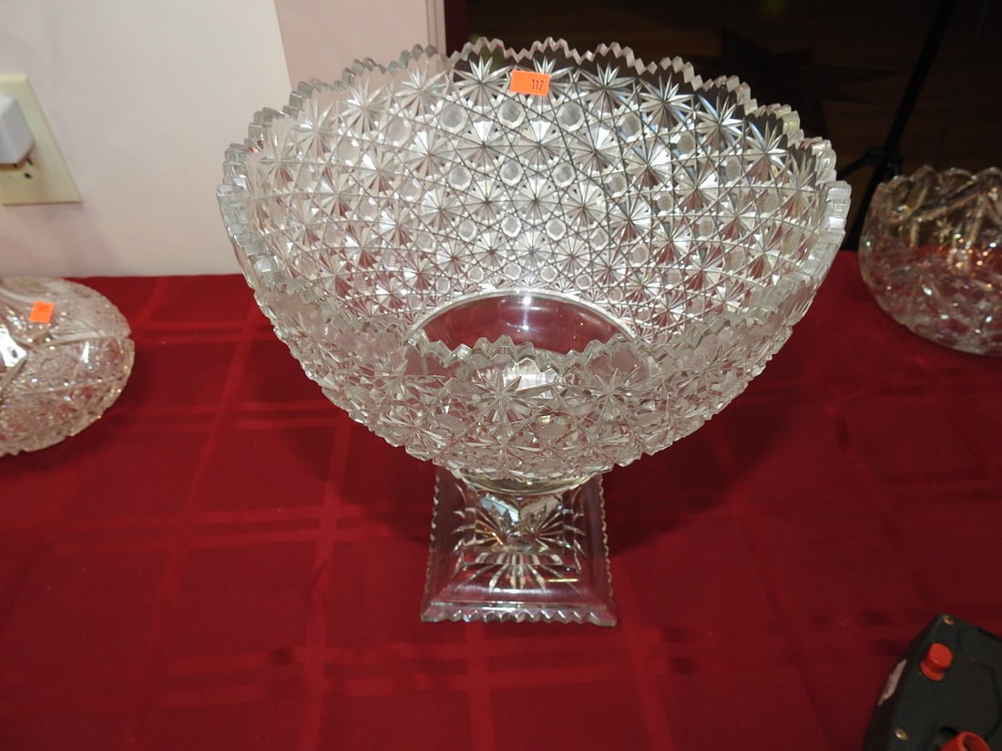 Large Pedestal Cut Glass Centerpiece Bowl: Large cut glass pedestal centerpiece or fruit bowl with tall foot, scalloped rim and deep geometric cutting. Approx. 11.5 x 9.5 x 9.5 in. Unmarked unless otherwise noted; maker/pattern attribution is