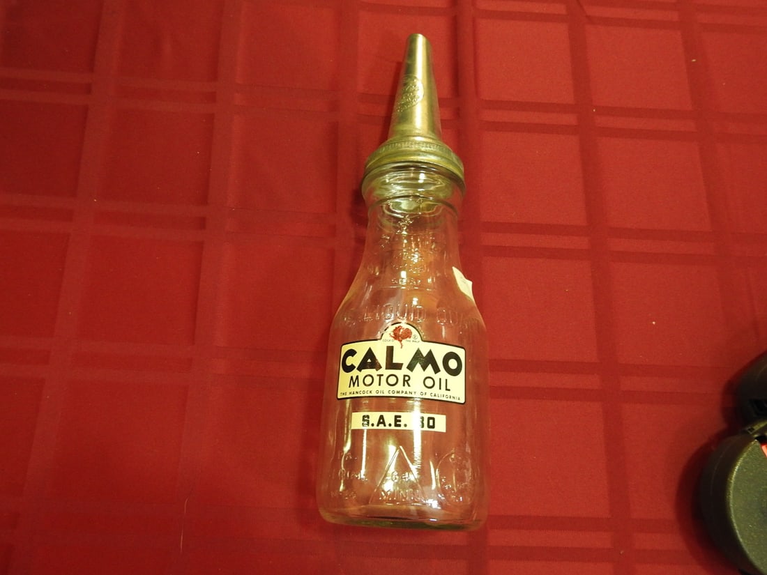 Calmo Motor Oil Glass Bottle with Spout: Antique quart glass oil bottle with Calmo Motor Oil label and metal spout. Approx. 13.5 x 3.75 x 3.75 in. Empty/decorative collectible; not tested for use. Shows age-related wear, patina, finish